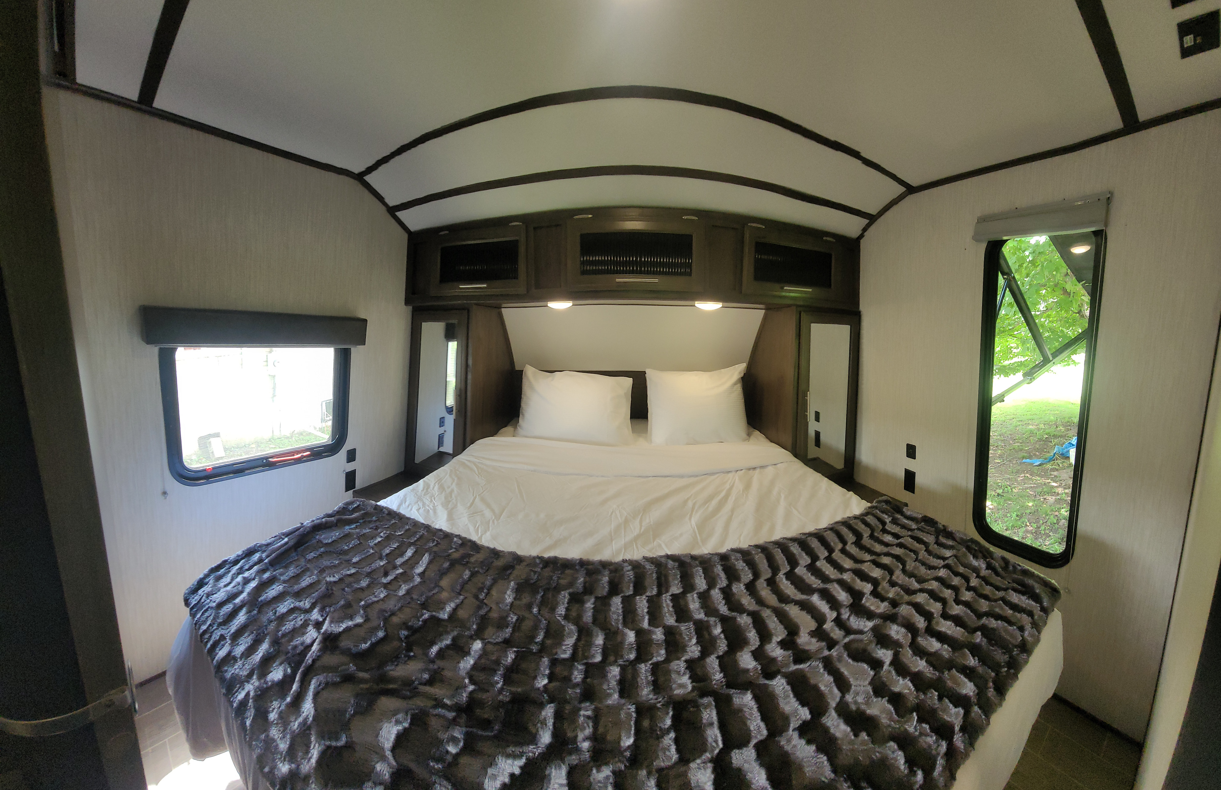 Cozy RV rental bedroom with a comfortable bed, overhead cabinets, and large windows offering scenic views for travel.. Forest River Cherokee Alpha Wolf 2020