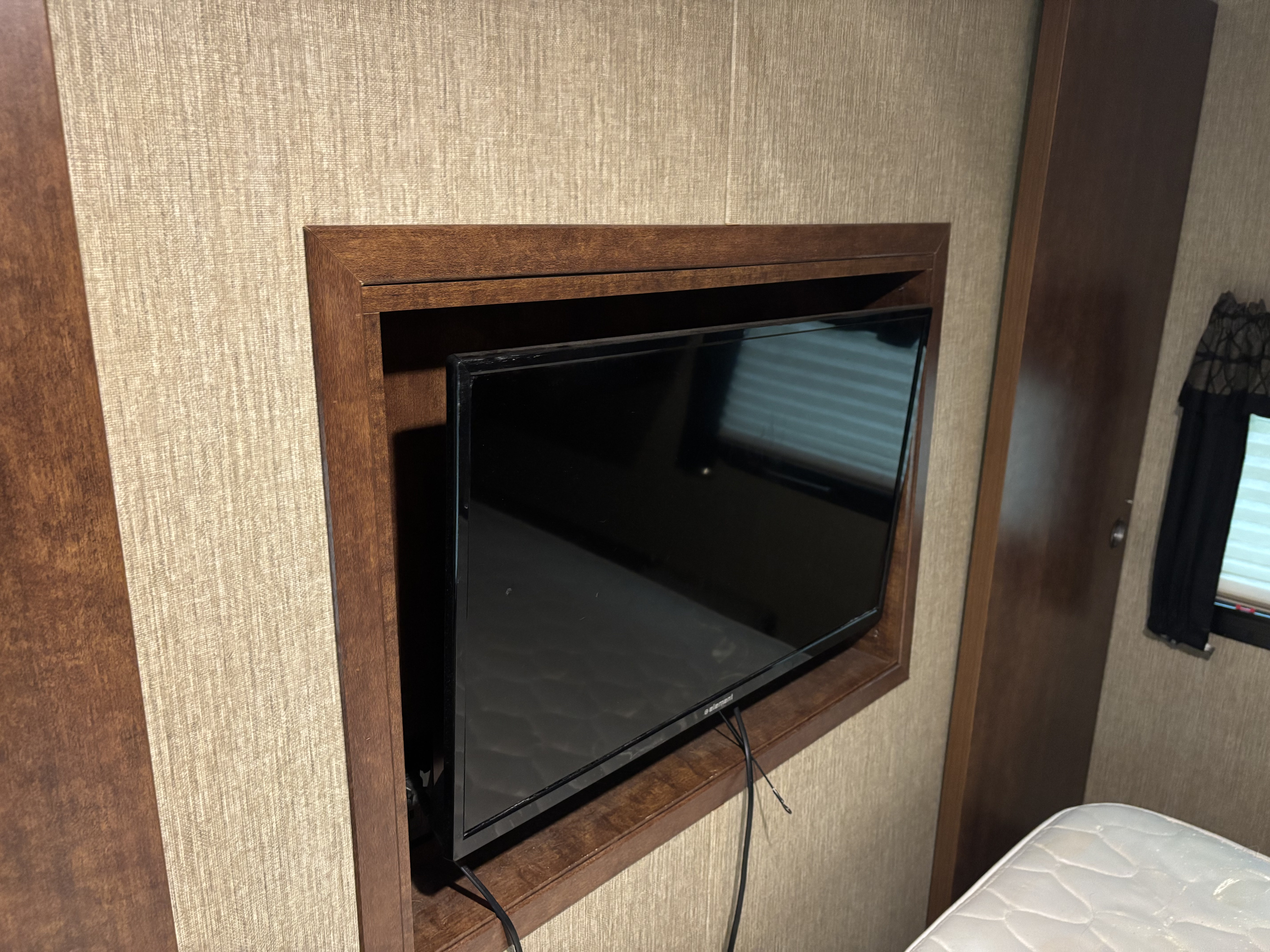 RV rental bedroom features a built-in TV in a wooden frame against textured walls. A glimpse of a mattress is visible.. Keystone RV Outback Ultra-Lite 2017