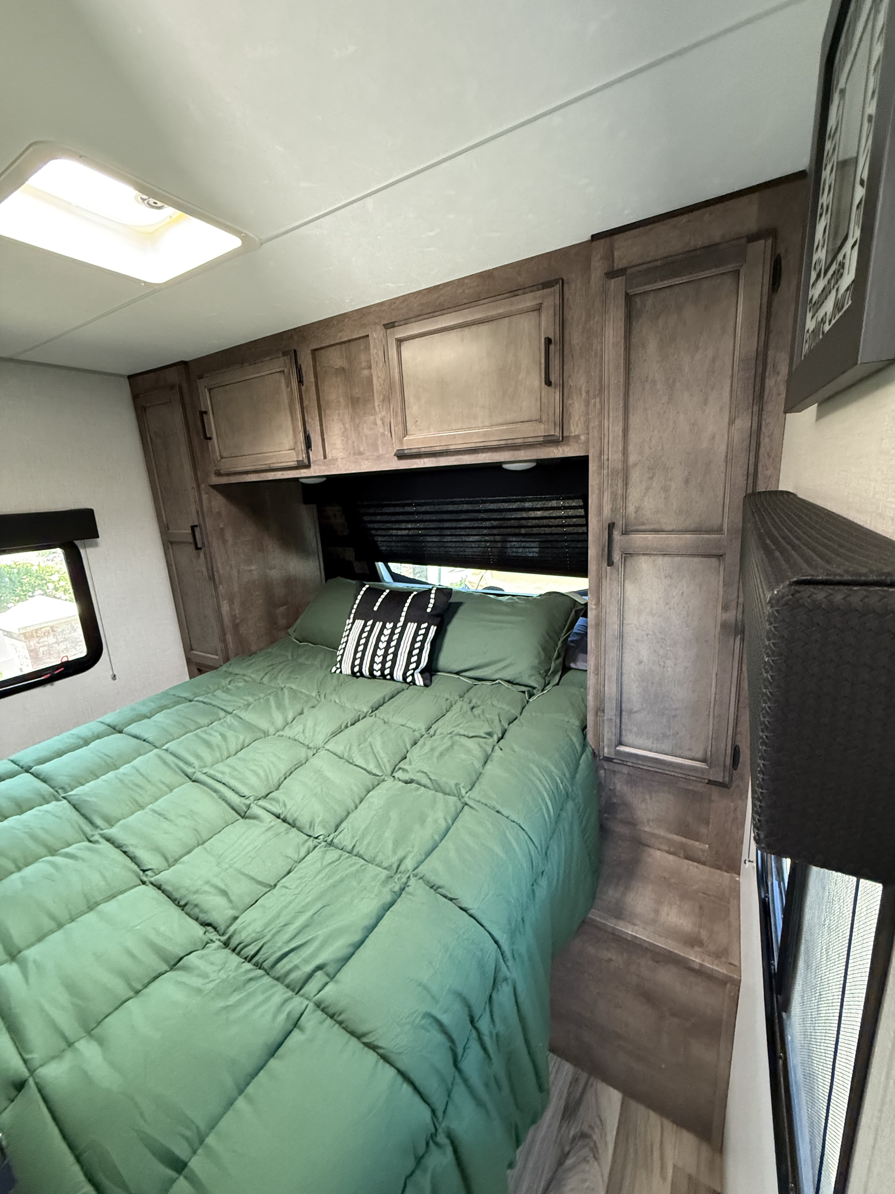 Cozy RV rental bedroom featuring a bed with a green comforter, decorative pillow, built-in cabinetry, and a window.. Sport Trek 270 VBH 2021