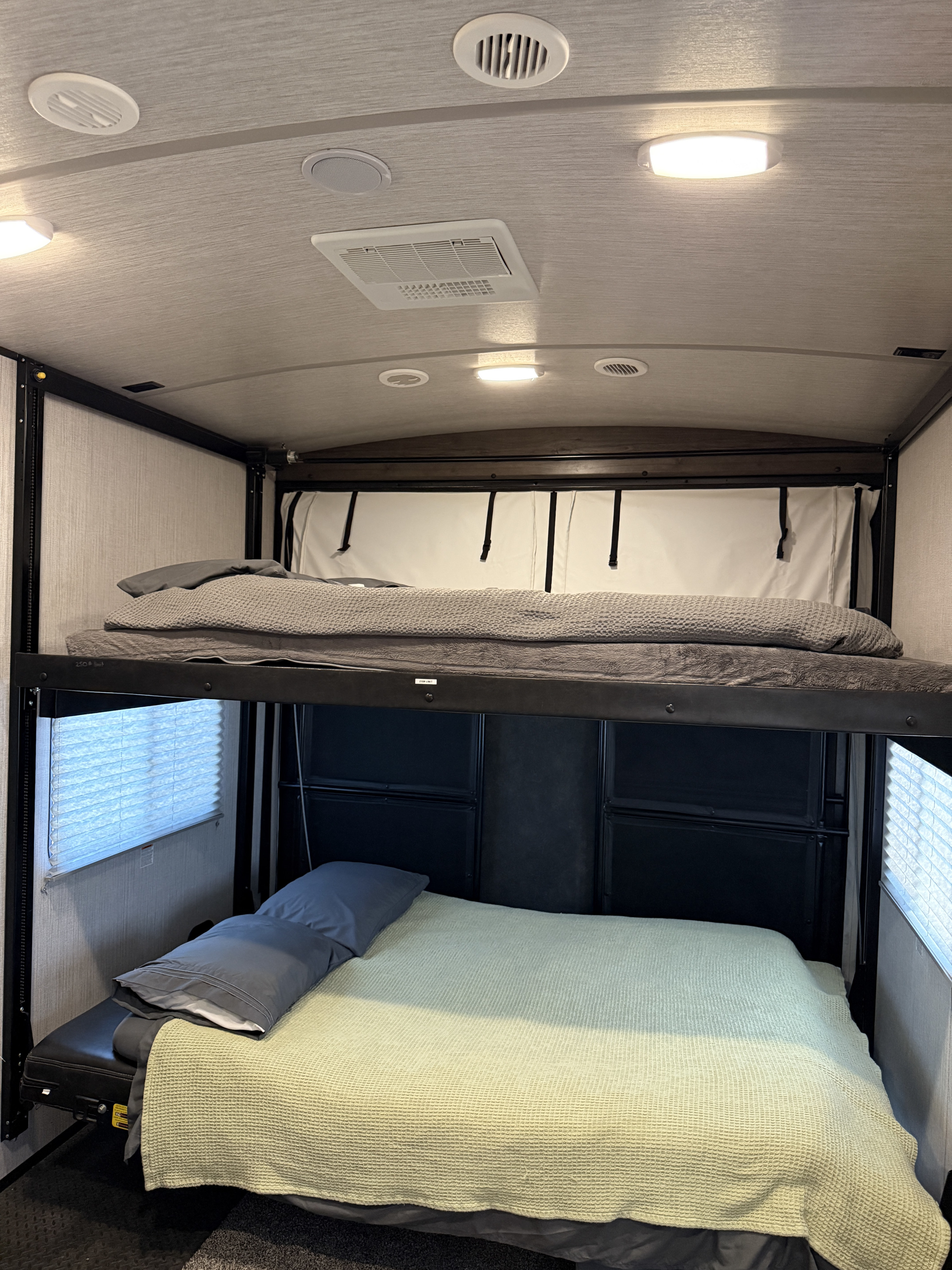 RV rental with two bunk beds ready for use, featuring comfortable bedding, a window with blinds, and ceiling fixtures.. Heartland Torque 2021