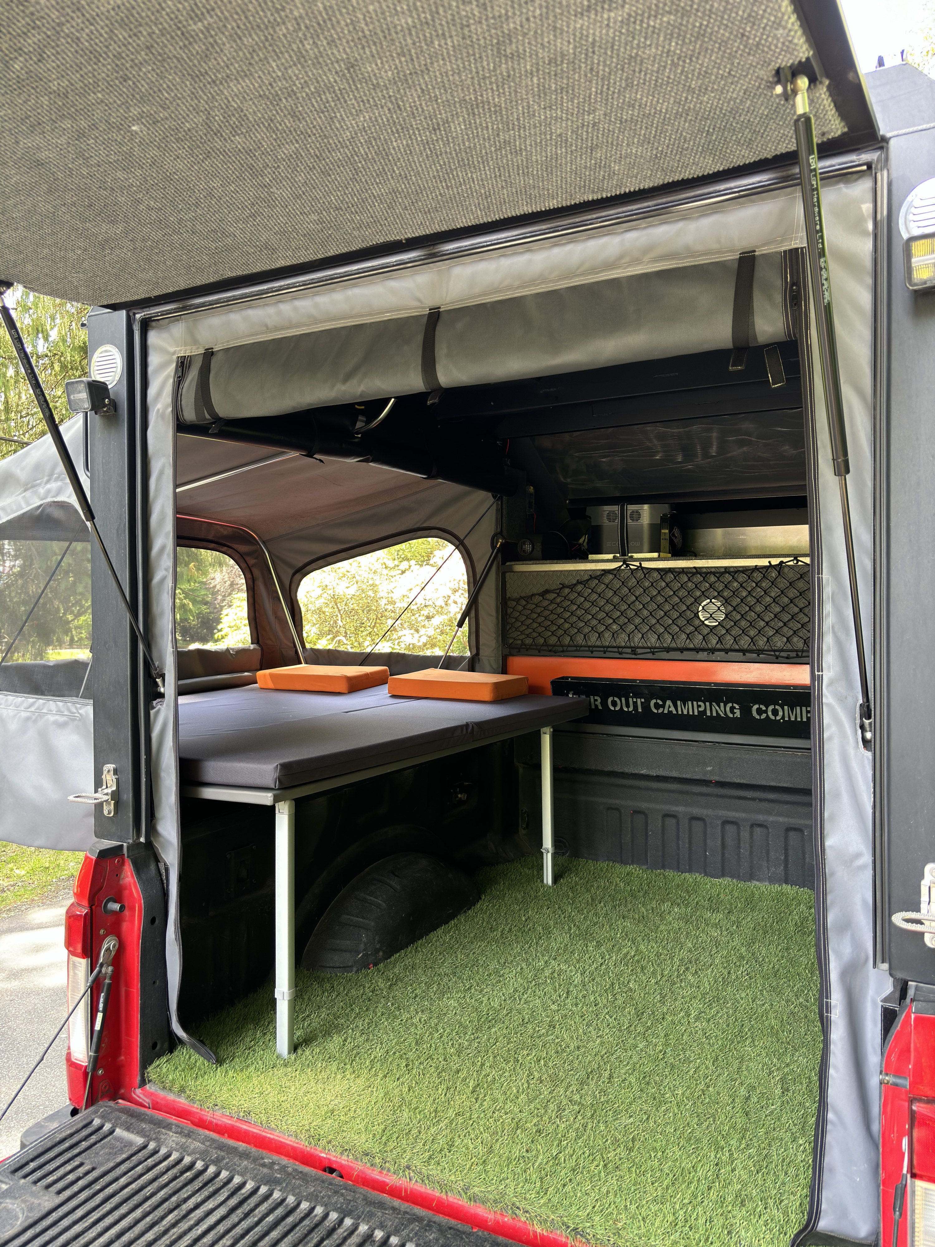Inside an RV rental truck camper: a cozy bed, handy storage, and artificial grass for comfortable outdoor adventures.. Far-Out Camper Far-Out Camper 6.5 ft 2024