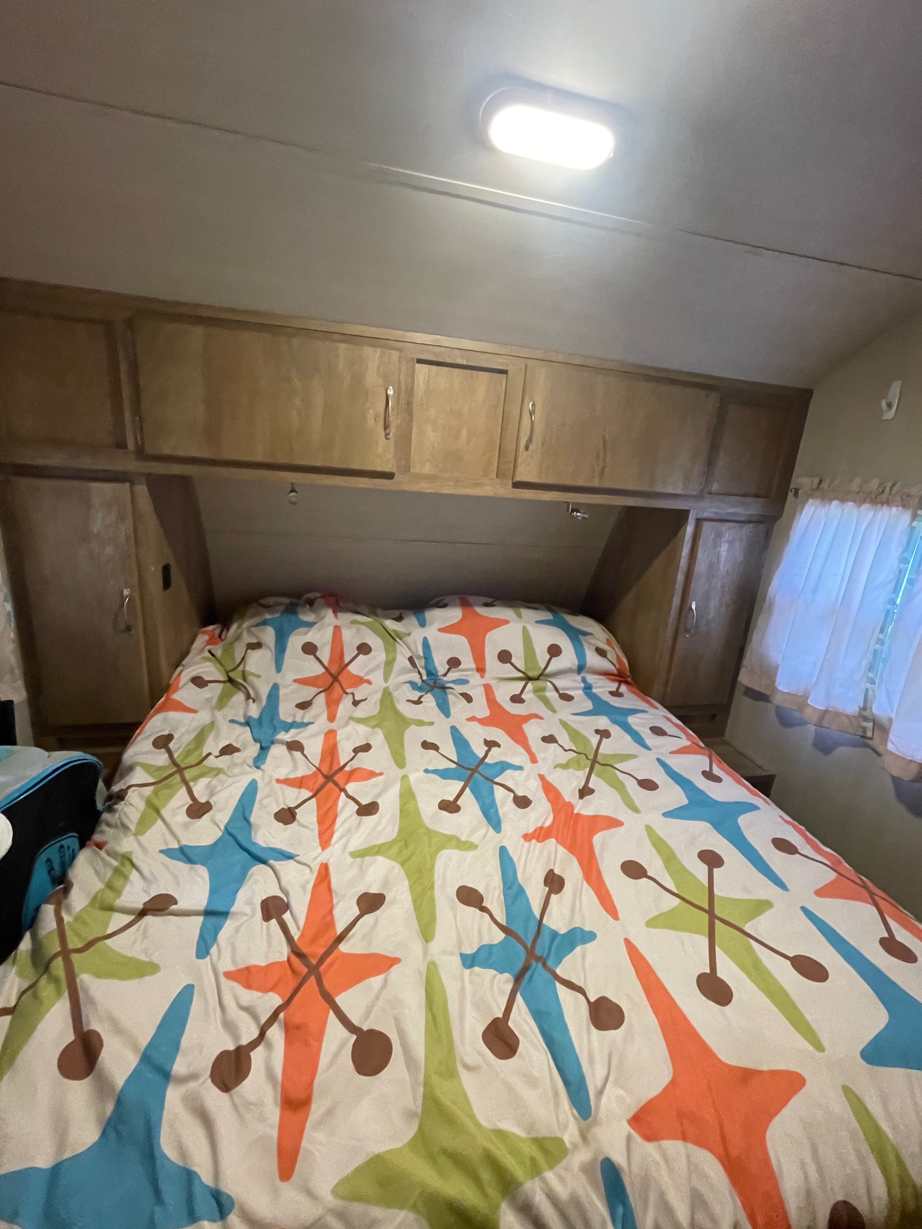 Cozy RV rental bedroom: bed with a mid-century modern duvet, overhead wooden cabinets, and bright ceiling light.. Gulf Stream Vintage Cruiser 2017