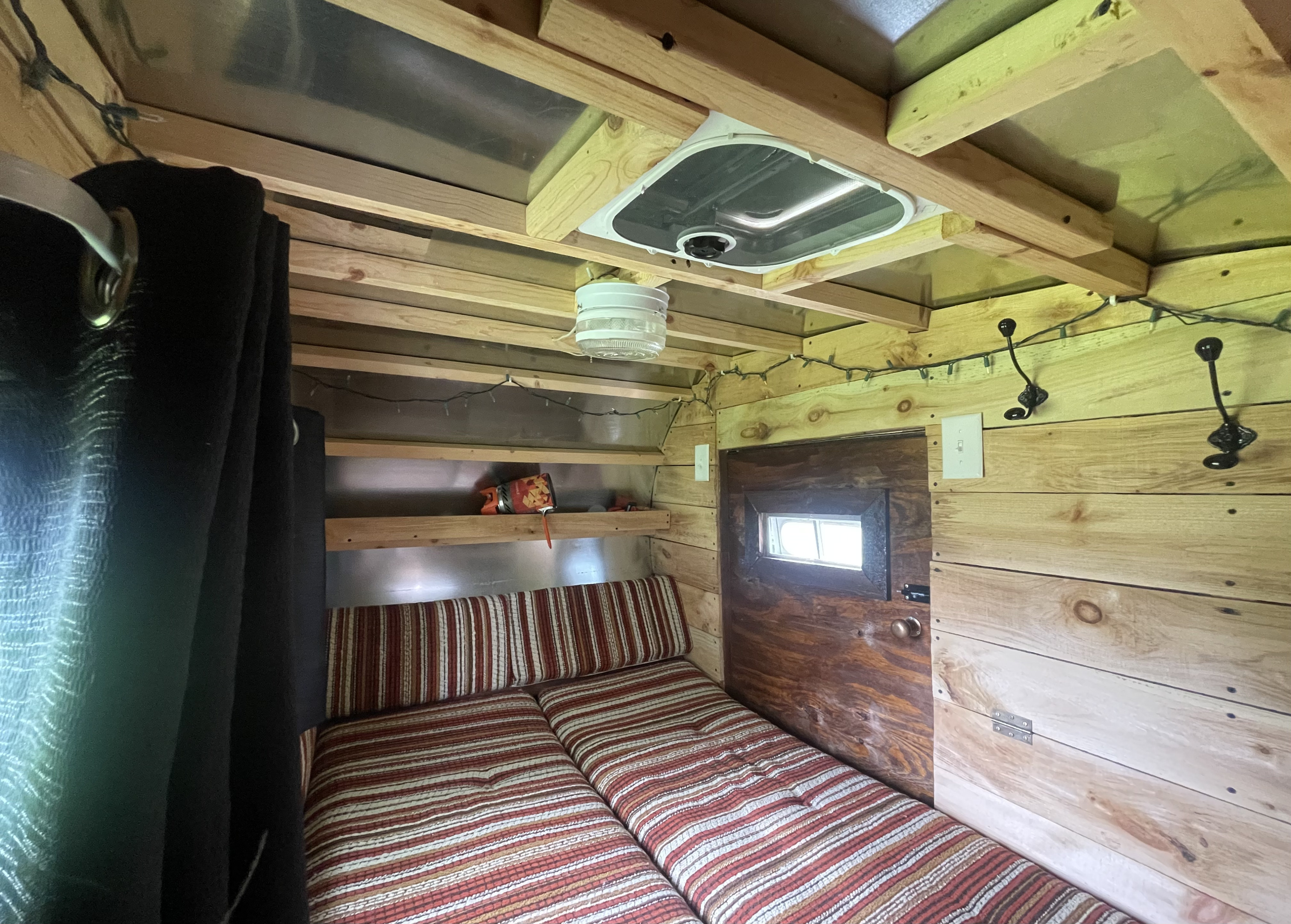 This inviting RV rental features a cozy striped bed, natural wood accents, shelves, and a ceiling fan.. Assembled Trailer 2024