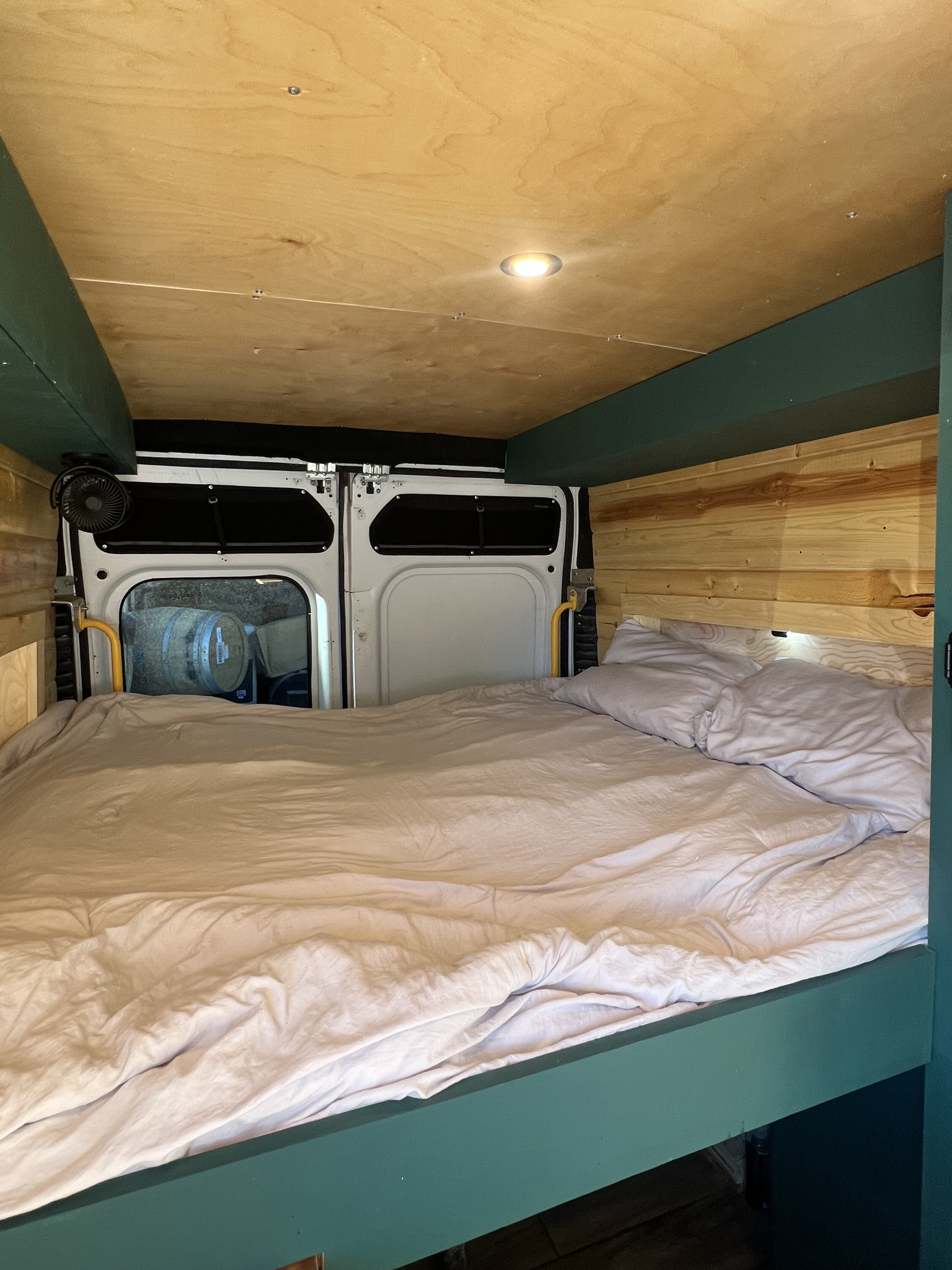 Inside a cozy camper van rv rental with a made bed, wooden walls & ceiling, and rear doors opening to barrels outside.. Dodge ProMaster 2500 2018