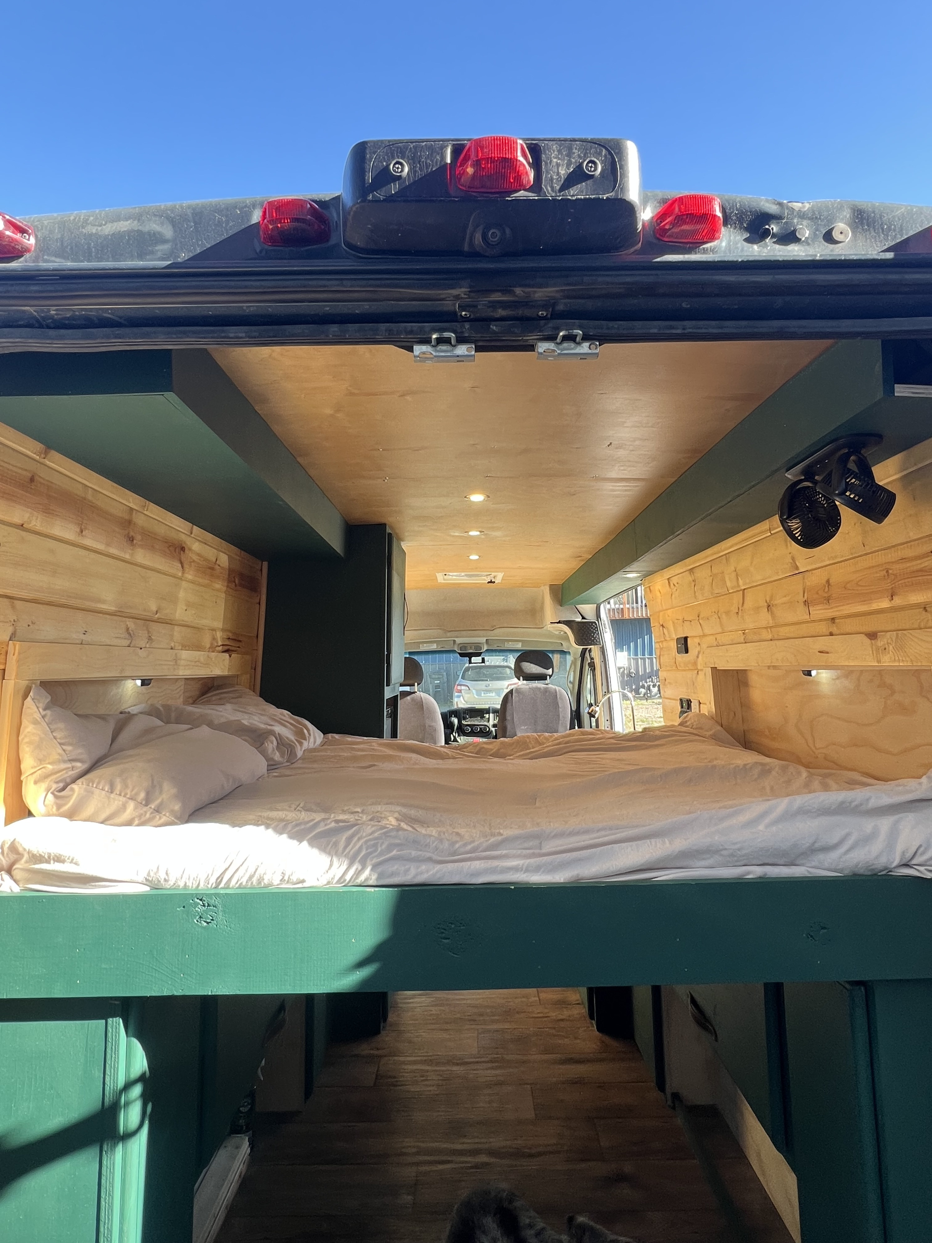 Cozy RV rental interior with a comfortable bed, wood paneling, and a view to the front cabin. Perfect for mobile adventures.. Dodge ProMaster 2500 2018