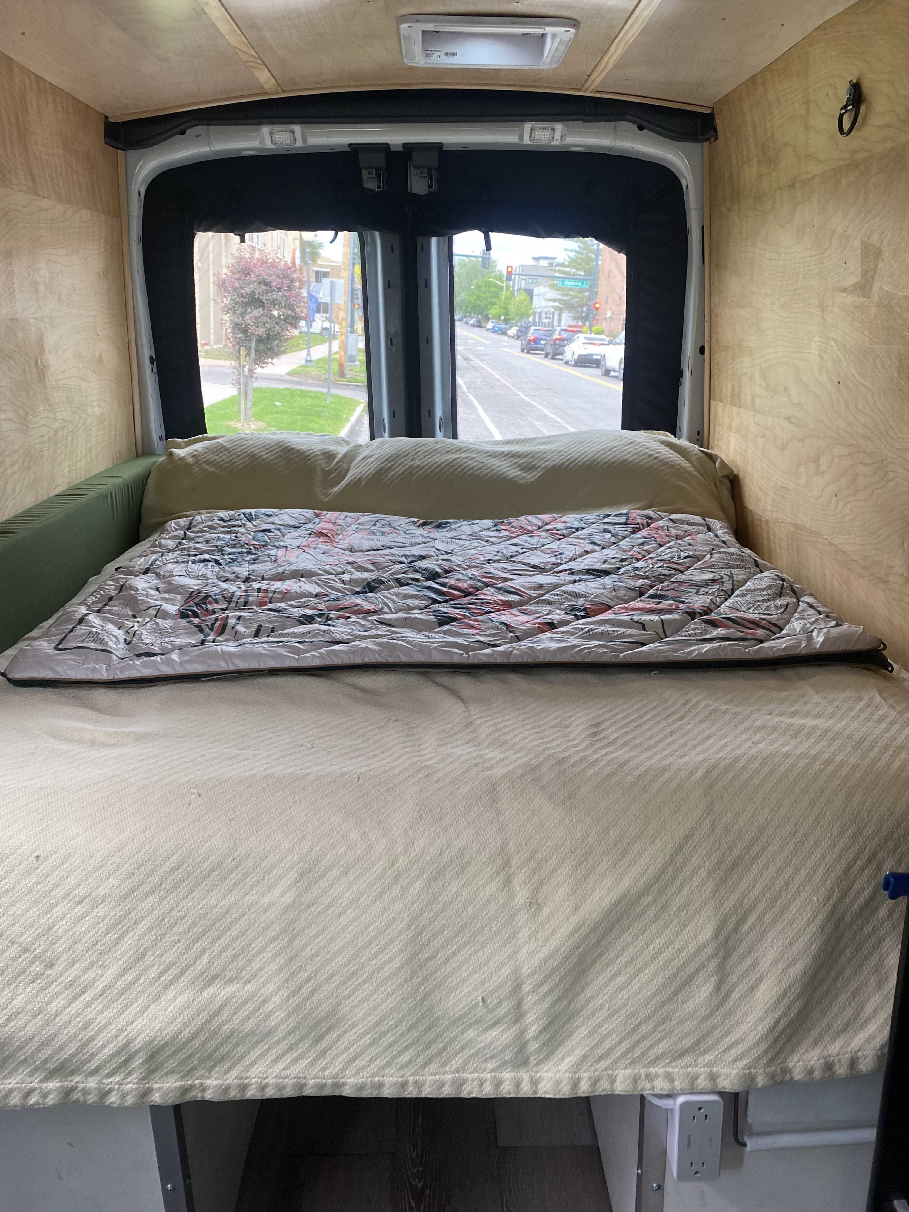 Inside an RV rental van: a comfy bed, wood-paneled interior, and a street view through the back windows.. Ford Transit 2018