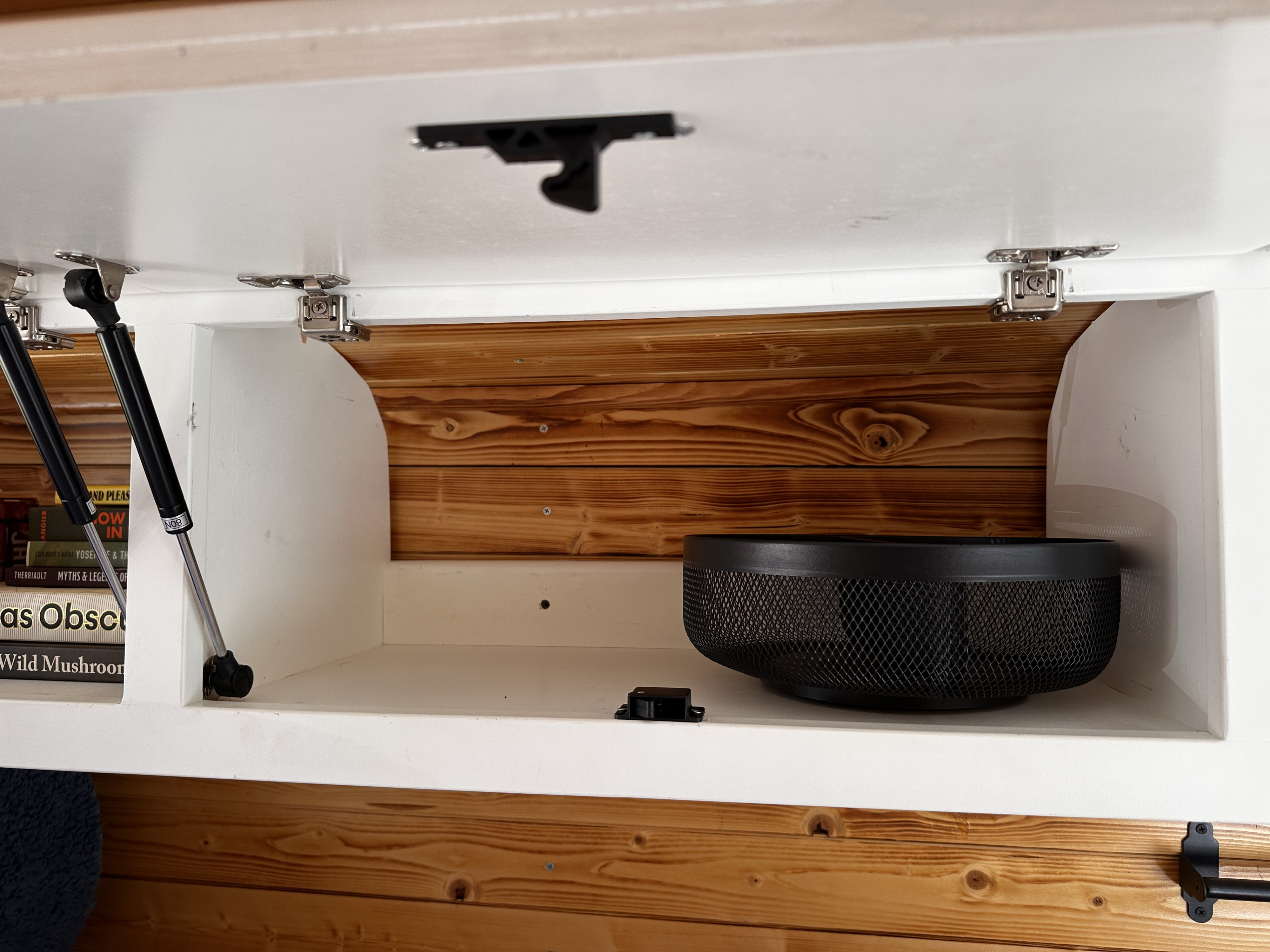 RV rental storage: open overhead cabinet with gas struts, books, and mesh bowl inside a wood-paneled interior.. Ford Transit 250 2015