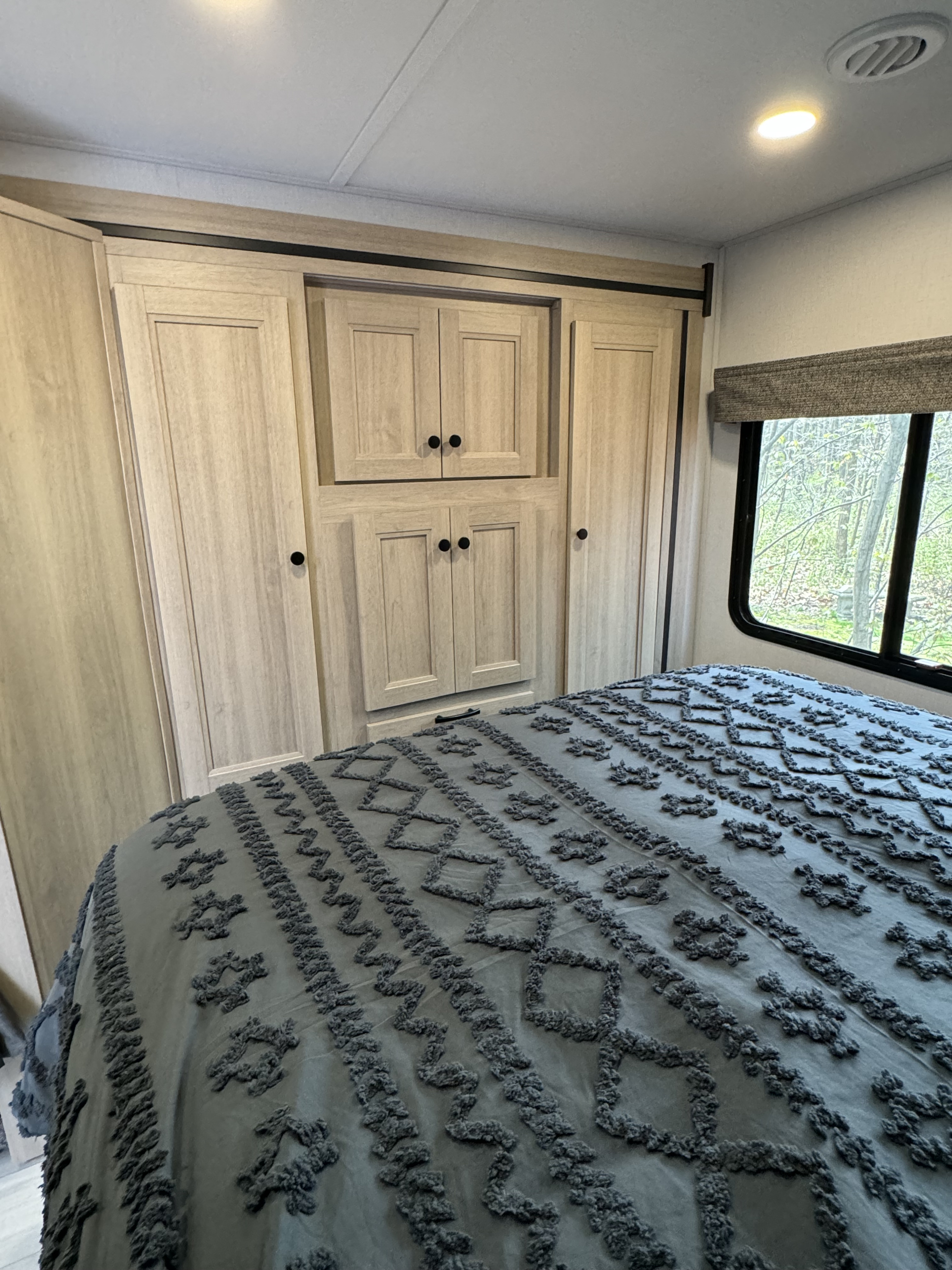 Inside an RV rental: a spacious bedroom with light wood cabinetry, a patterned comforter on the bed, and a scenic window.. Forest River 3251DSLE 2025