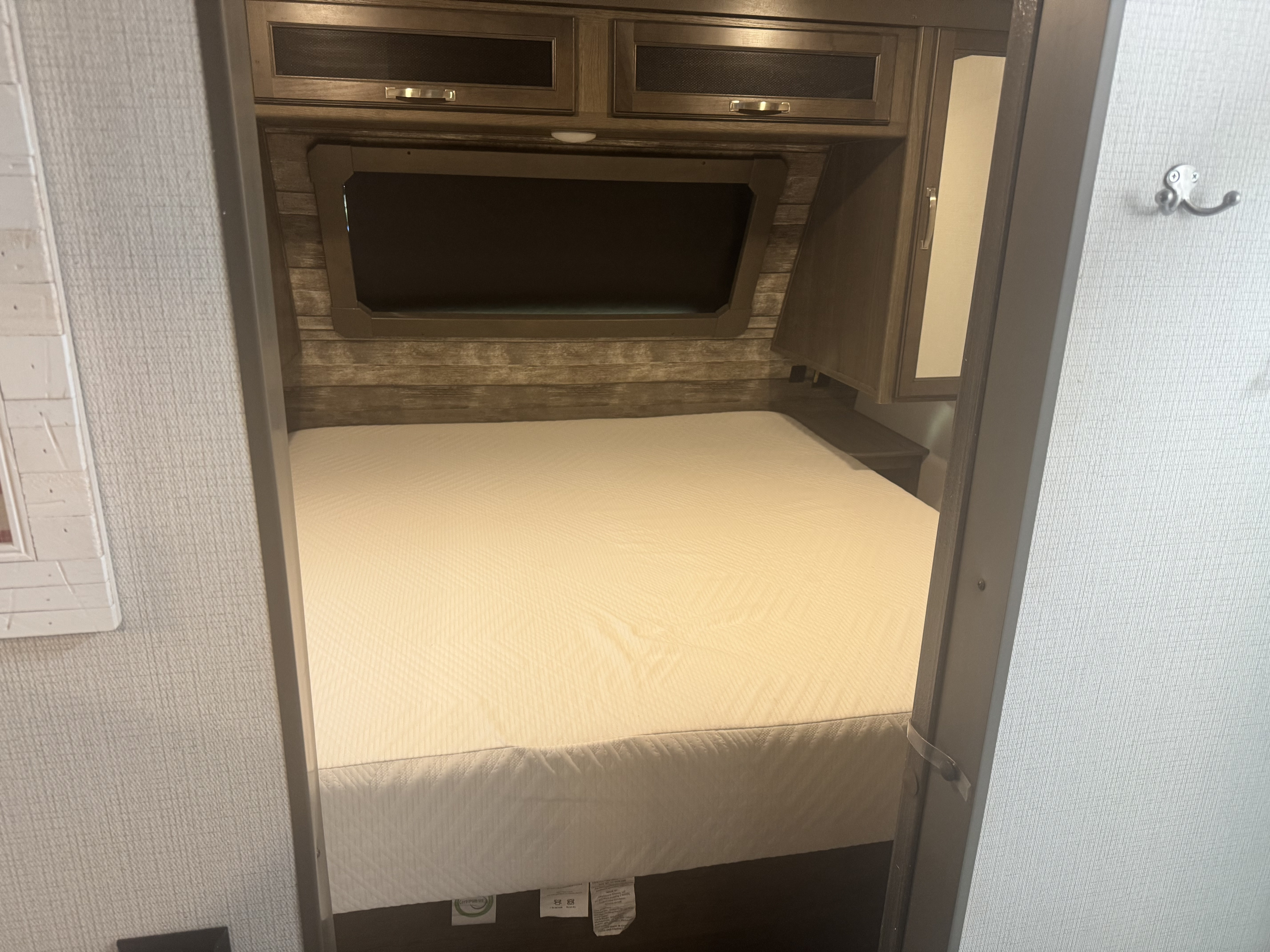 Step into this compact RV rental bedroom, featuring a new mattress, wood-paneled headboard, and overhead cabinets.. Keystone RV Cougar 2022