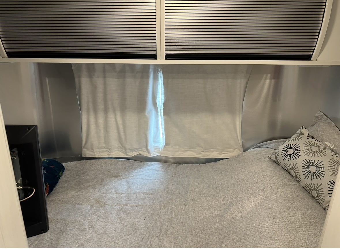 Inside a comfy RV rental: a bright sleeping area with a light grey bed, pillows, and privacy curtains.. Airstream Bambi 2022