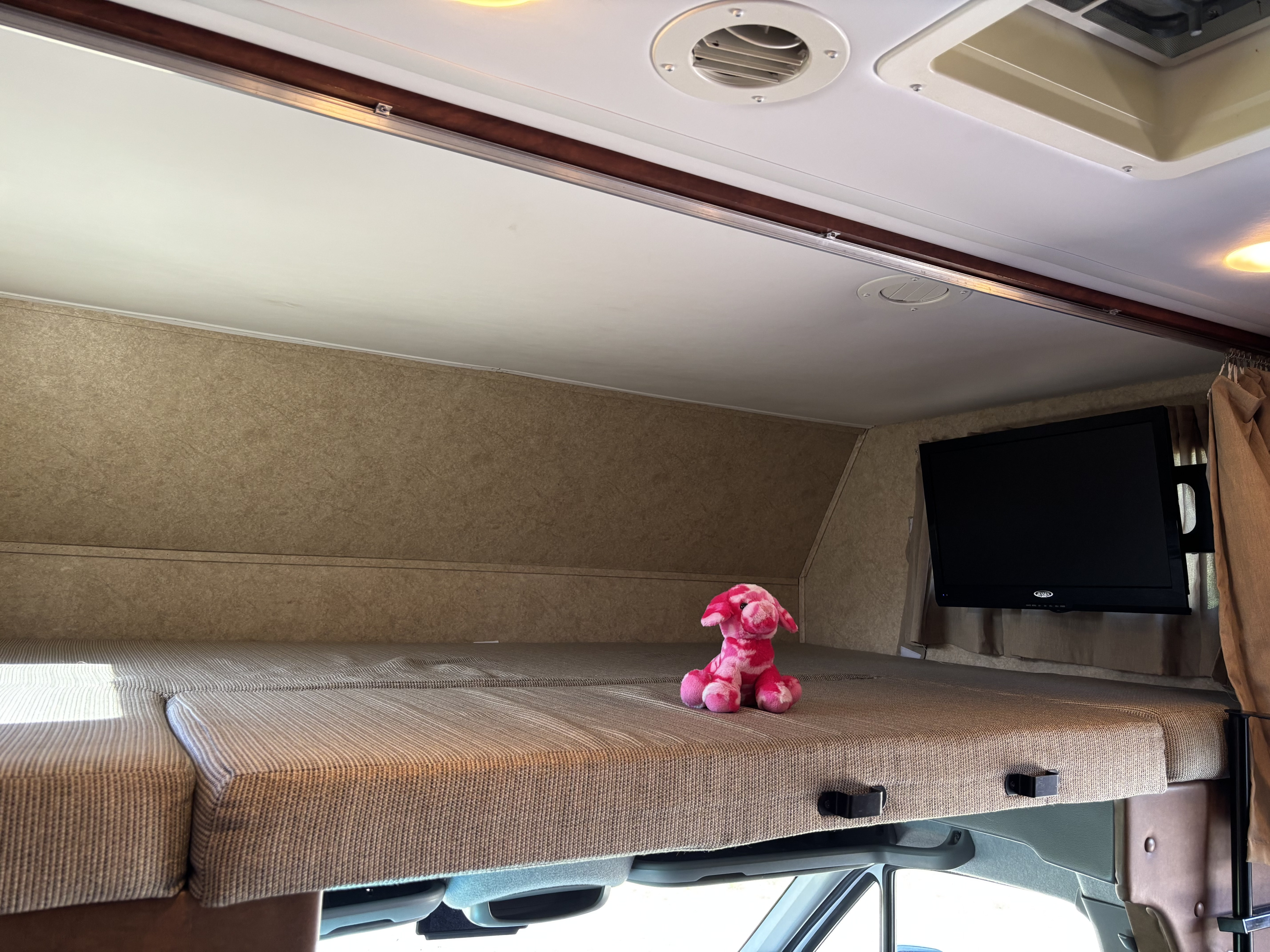 Cozy RV rental cab-over bunk with striped mattress, mounted TV, and a pink stuffed animal. Ready for adventure!. Forest River Solera 2013