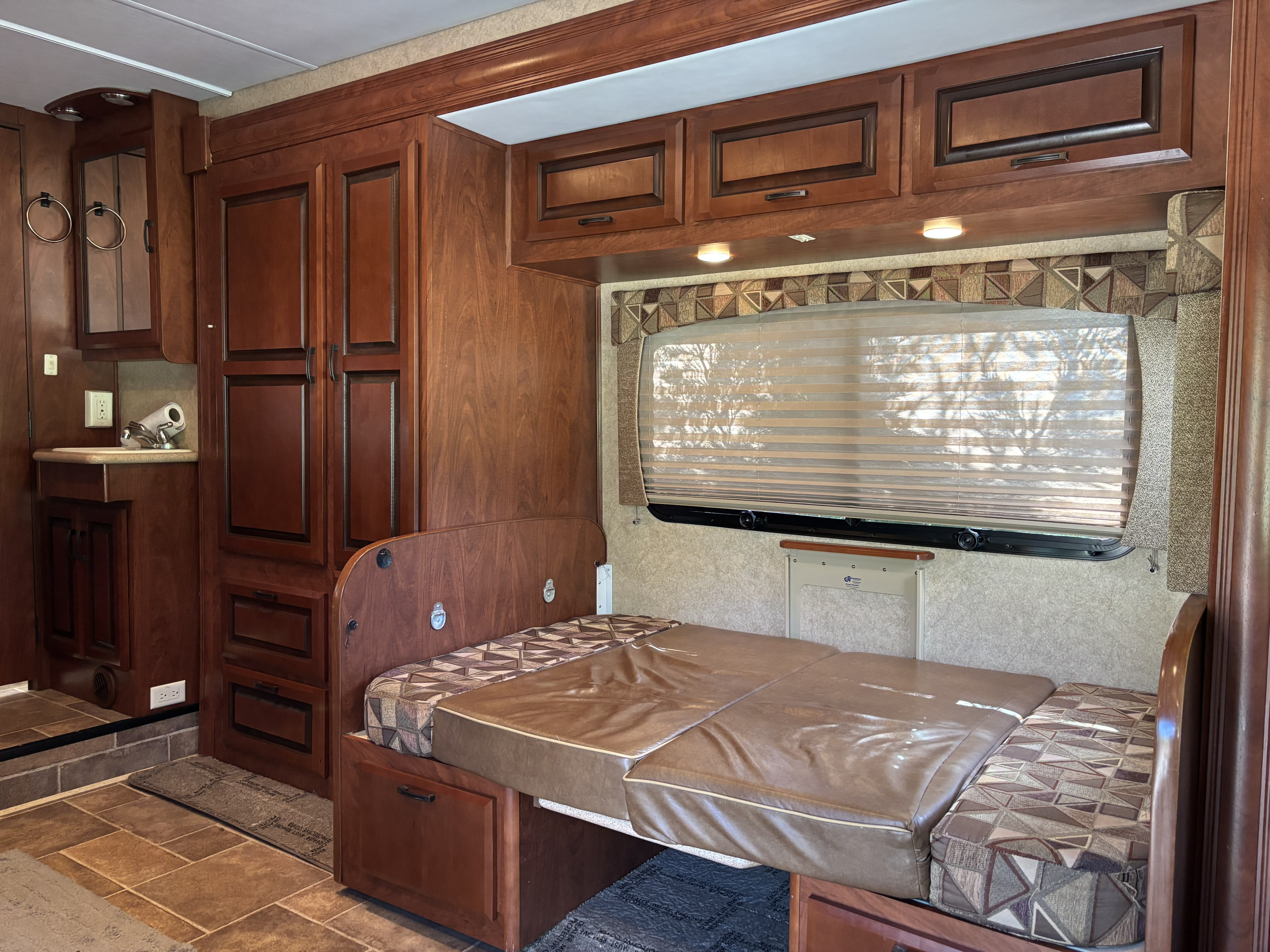RV rental interior showing dark wood cabinets, a convertible bed, sink, and window with blinds.. Forest River Solera 2013