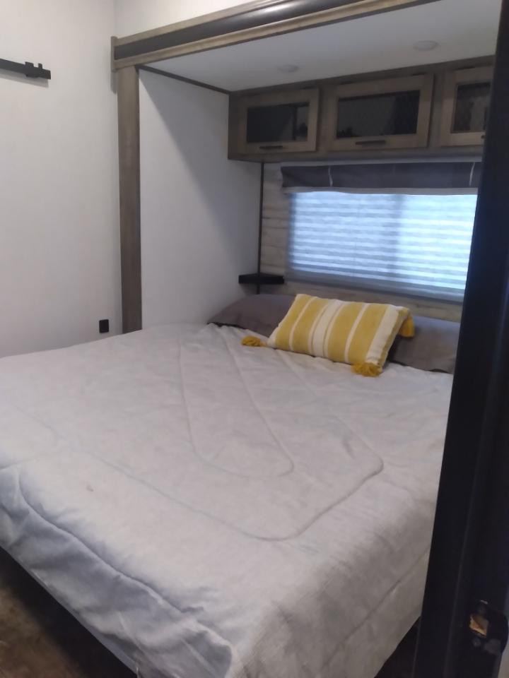 RV rental bedroom with a comfy bed, overhead cabinets, and a window with blinds, ready for a relaxing stay.. Forest River Sabre 2022