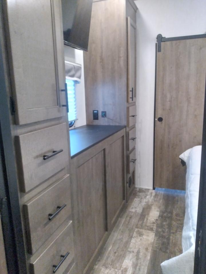 Modern RV rental interior with light wood cabinets, dark counter, mounted TV, and a barn door leading to the bedroom.. Forest River Sabre 2022