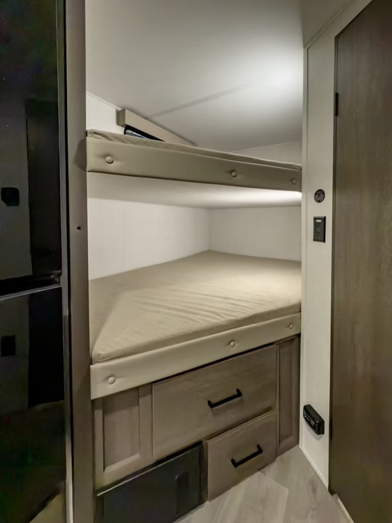 Inside an RV rental: functional bunk beds with built-in storage drawers below, designed for comfortable travel and space efficiency.. Grand Design Transcend 2025