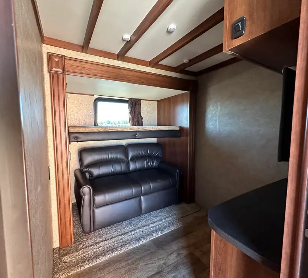Cozy RV rental interior with a black leather sofa, overhead bunk bed, and wooden beamed ceiling.. Jayco Eagle 2018