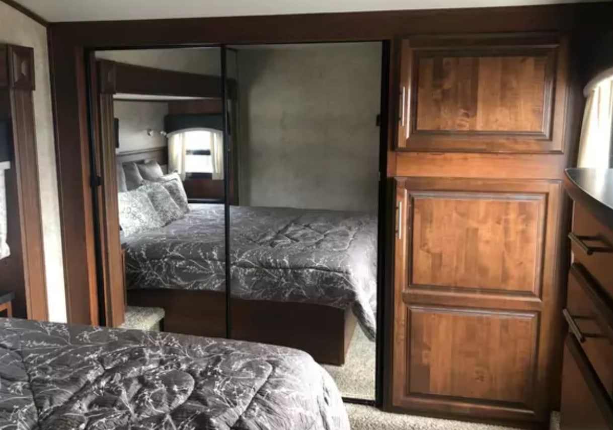 An RV rental bedroom with a gray patterned bed, large mirrored closet, and rich wood cabinetry.. Jayco Eagle 2018