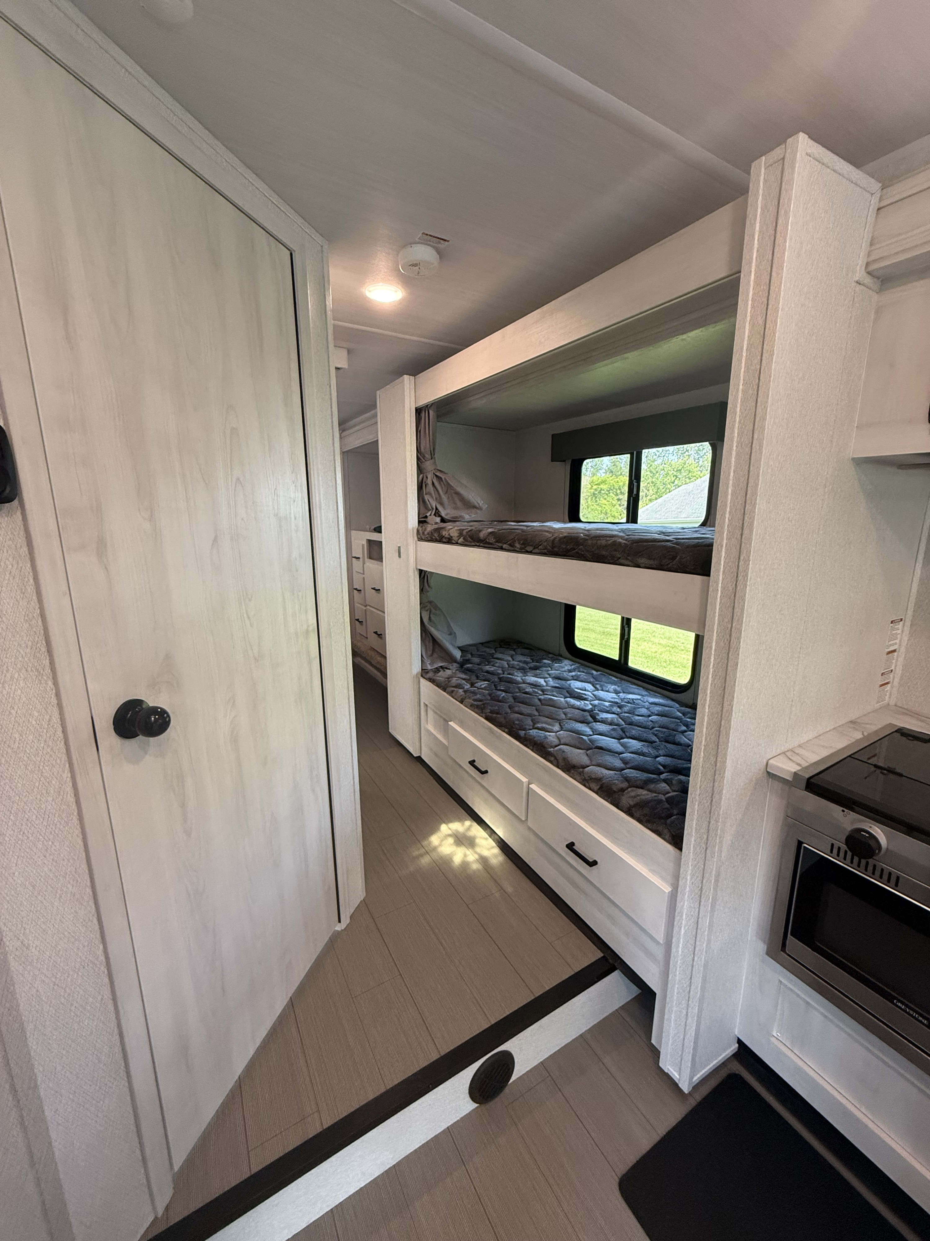 Discover this modern RV rental interior, showcasing bunk beds, a compact kitchen, and bright natural light through windows.. Forest River East to West Entrada 2024