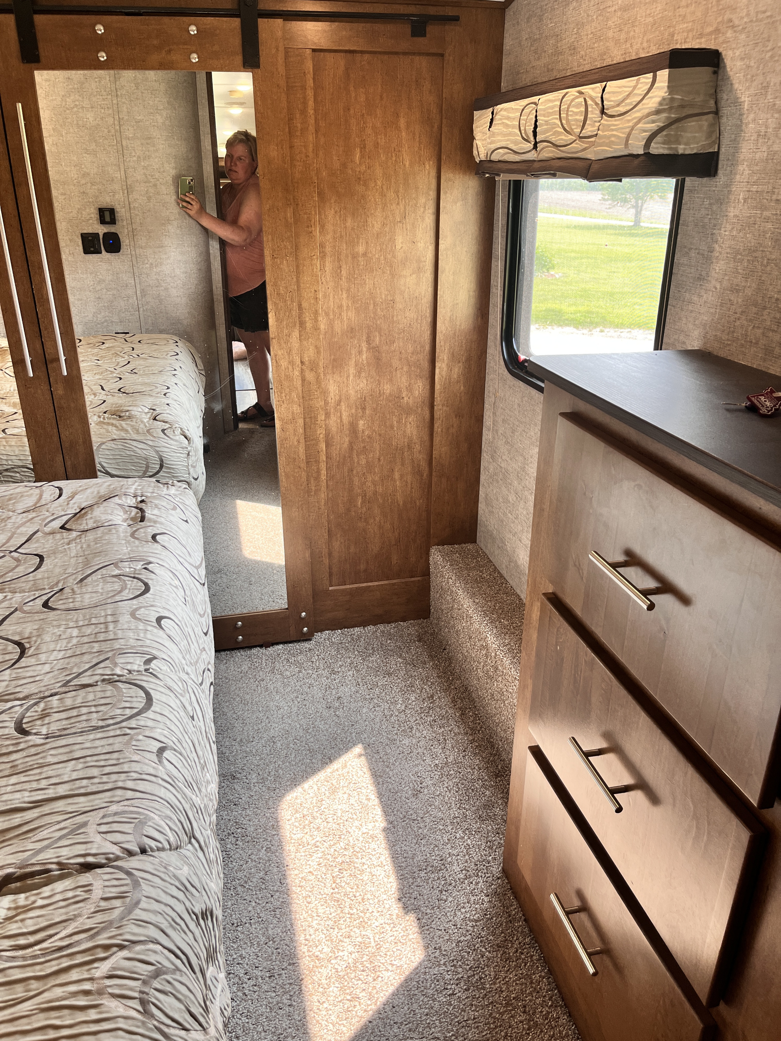 An RV rental bedroom with two comfy beds, a mirrored closet door, and a wooden dresser by the window.. Forest River Sabre 2019