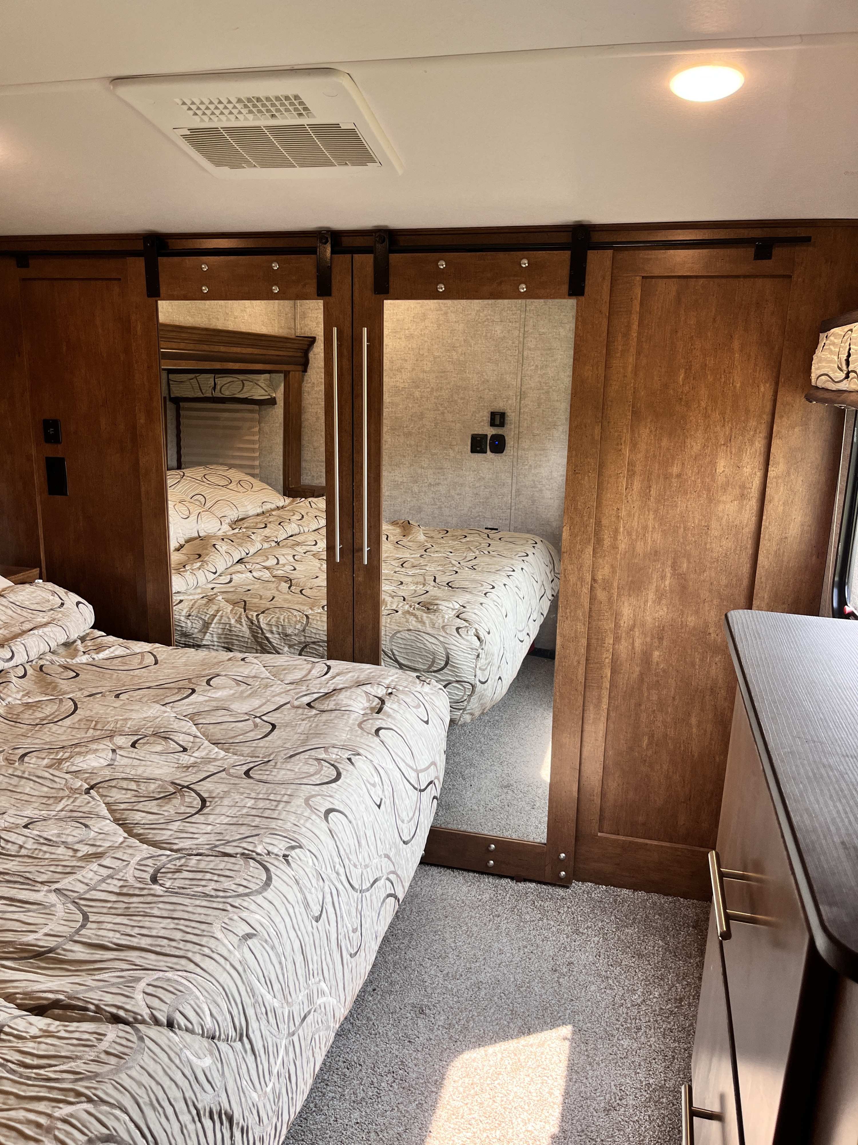 Cozy RV rental bedroom with patterned bedding on the bed, mirrored closet doors, and rich wood cabinetry.. Forest River Sabre 2019