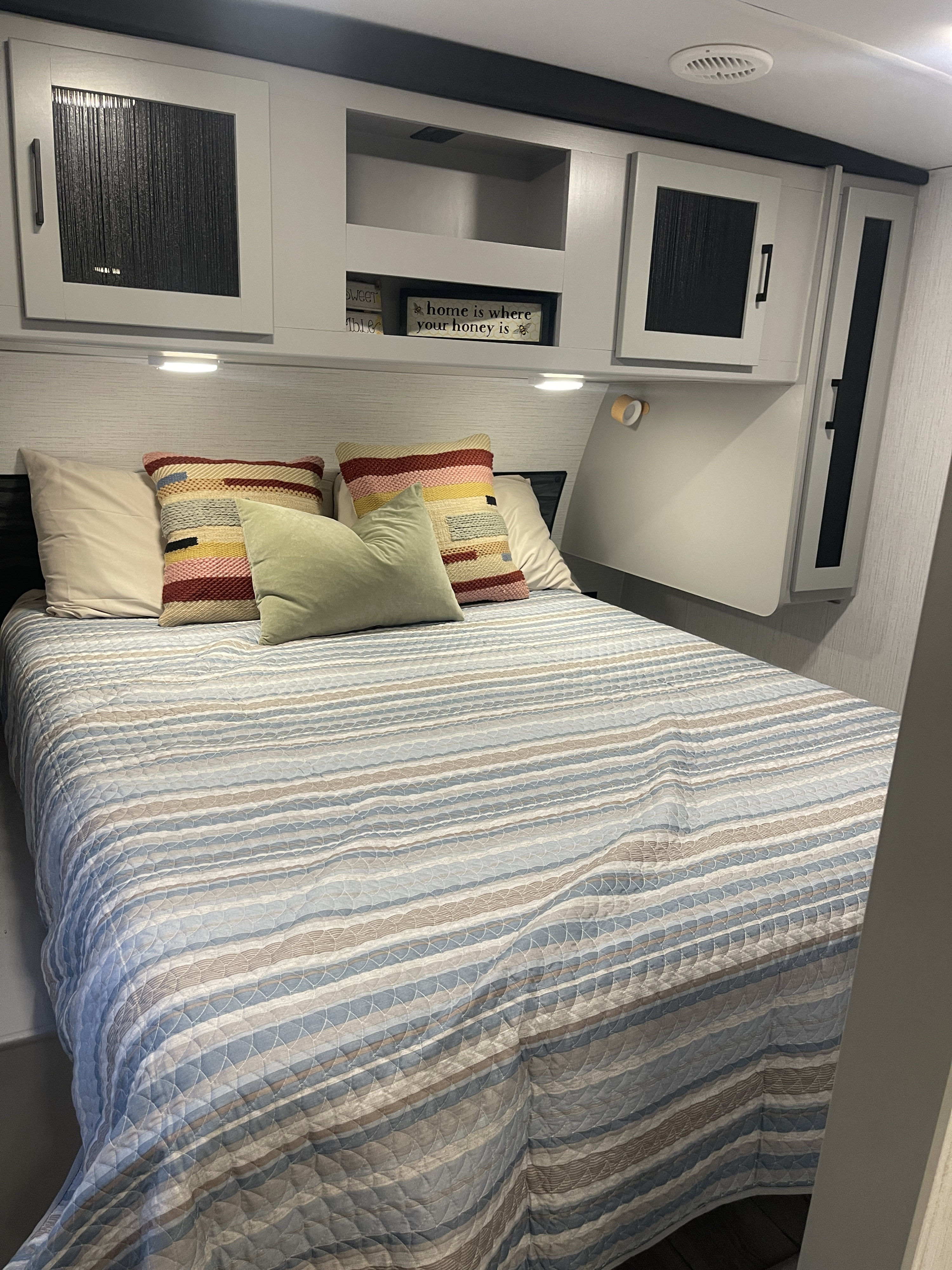 Cozy RV rental bedroom featuring a bed with a quilted striped comforter, colorful pillows, and ample overhead storage.. Heartland RVs North Trail 2023