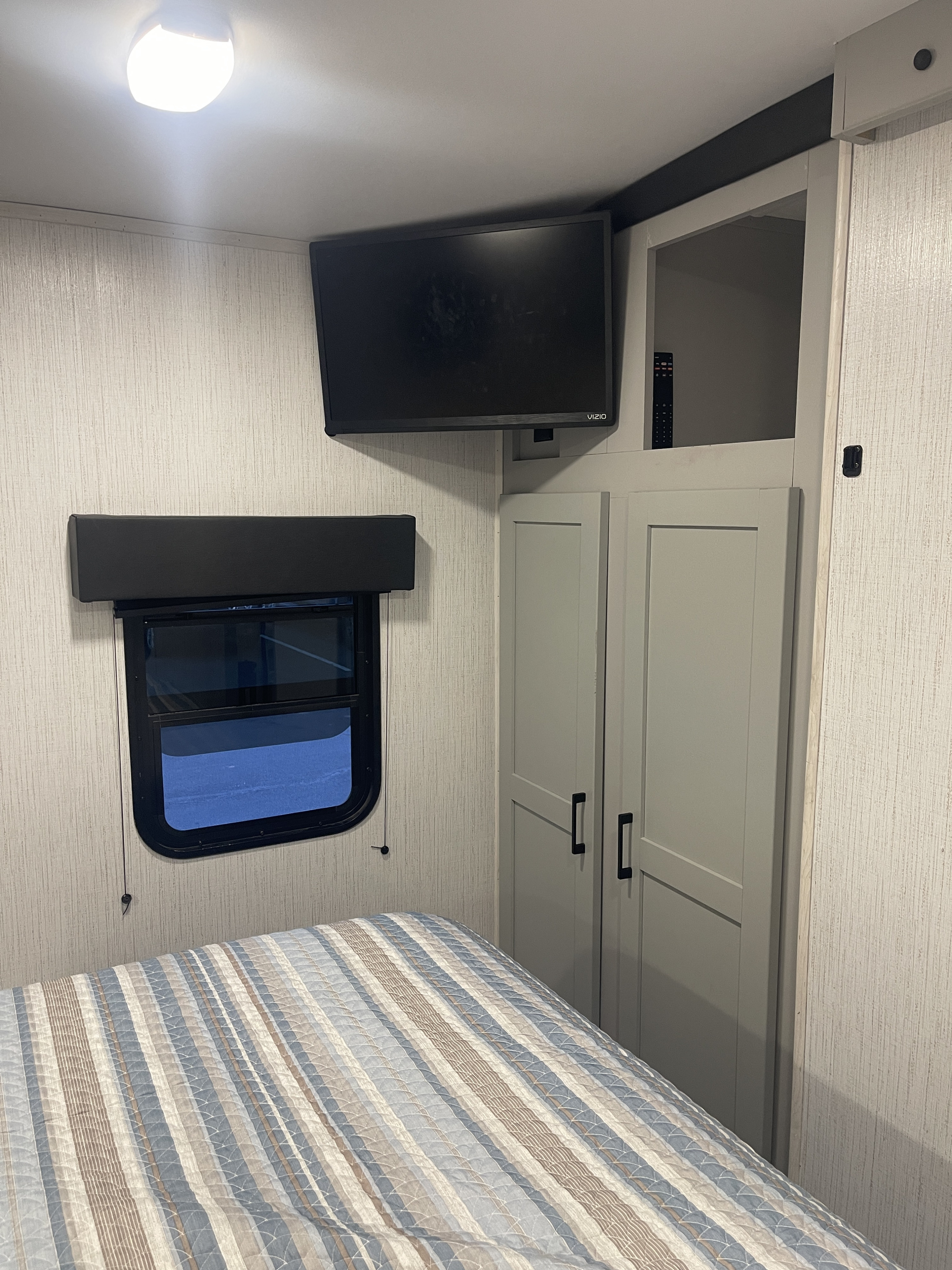 Cozy RV rental bedroom featuring a striped bed, wall TV, window, and storage cabinets for comfortable travel.. Heartland RVs North Trail 2023