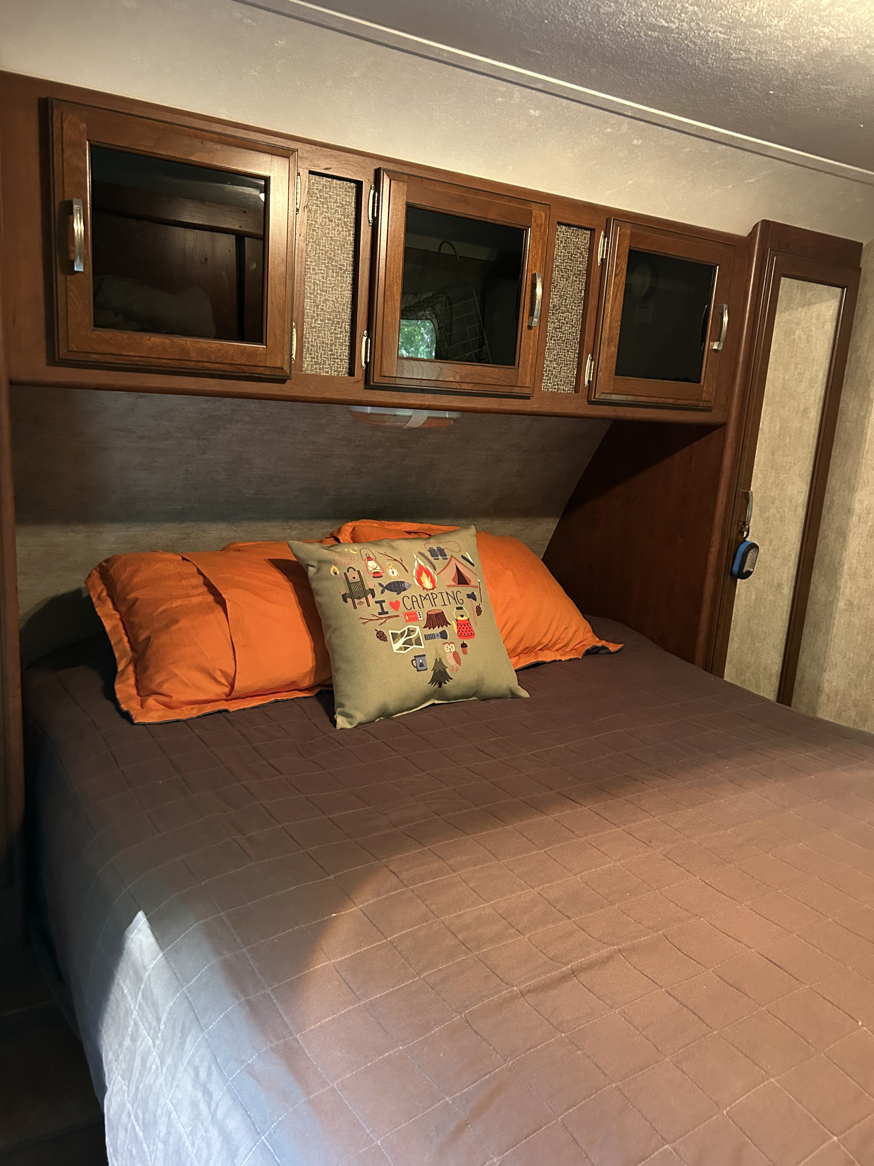 Cozy RV rental bedroom with overhead cabinets, an "I ❤️ Camping" pillow, and a brown quilted bed.. Keystone RV Passport Grand Touring 2015