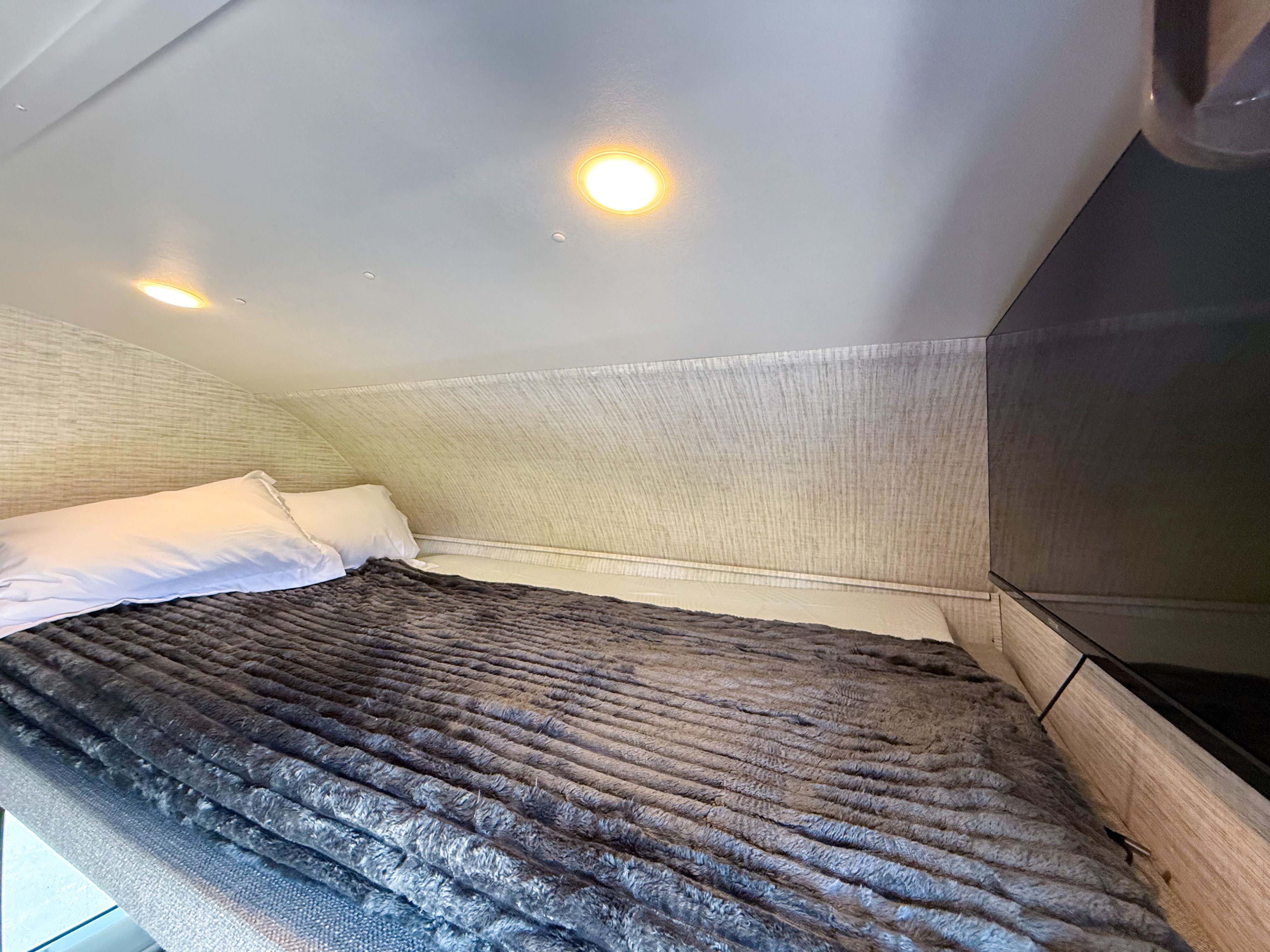 Inside an rv rental: a cozy bedroom with a plush gray blanket, white pillows, and a TV for comfort.. Entegra Odyssey SE 2025