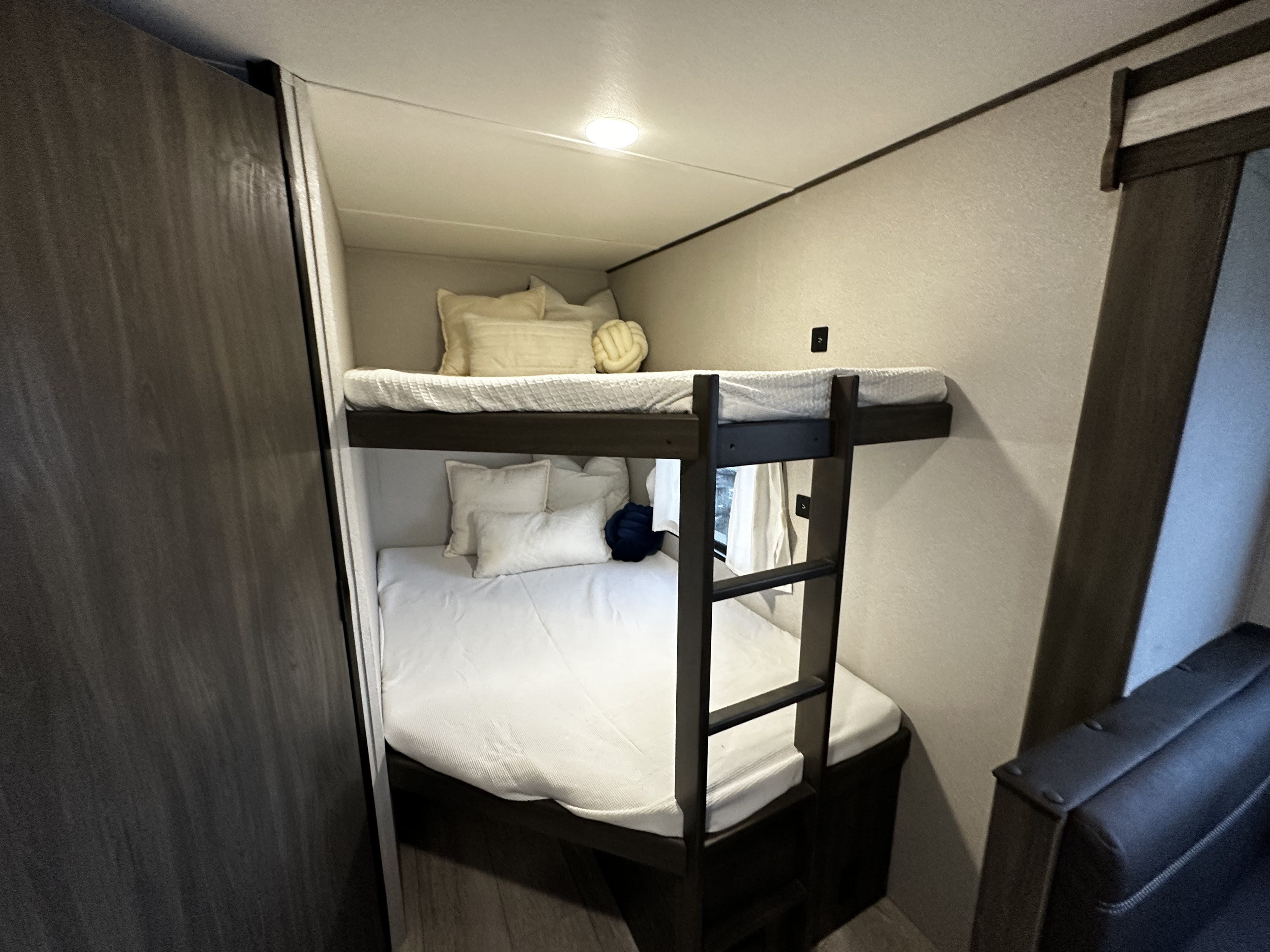 Cozy bunk beds in an RV rental, featuring white bedding, pillows, and a ladder in a compact space.. Forest River Grand River Comfortline 2021