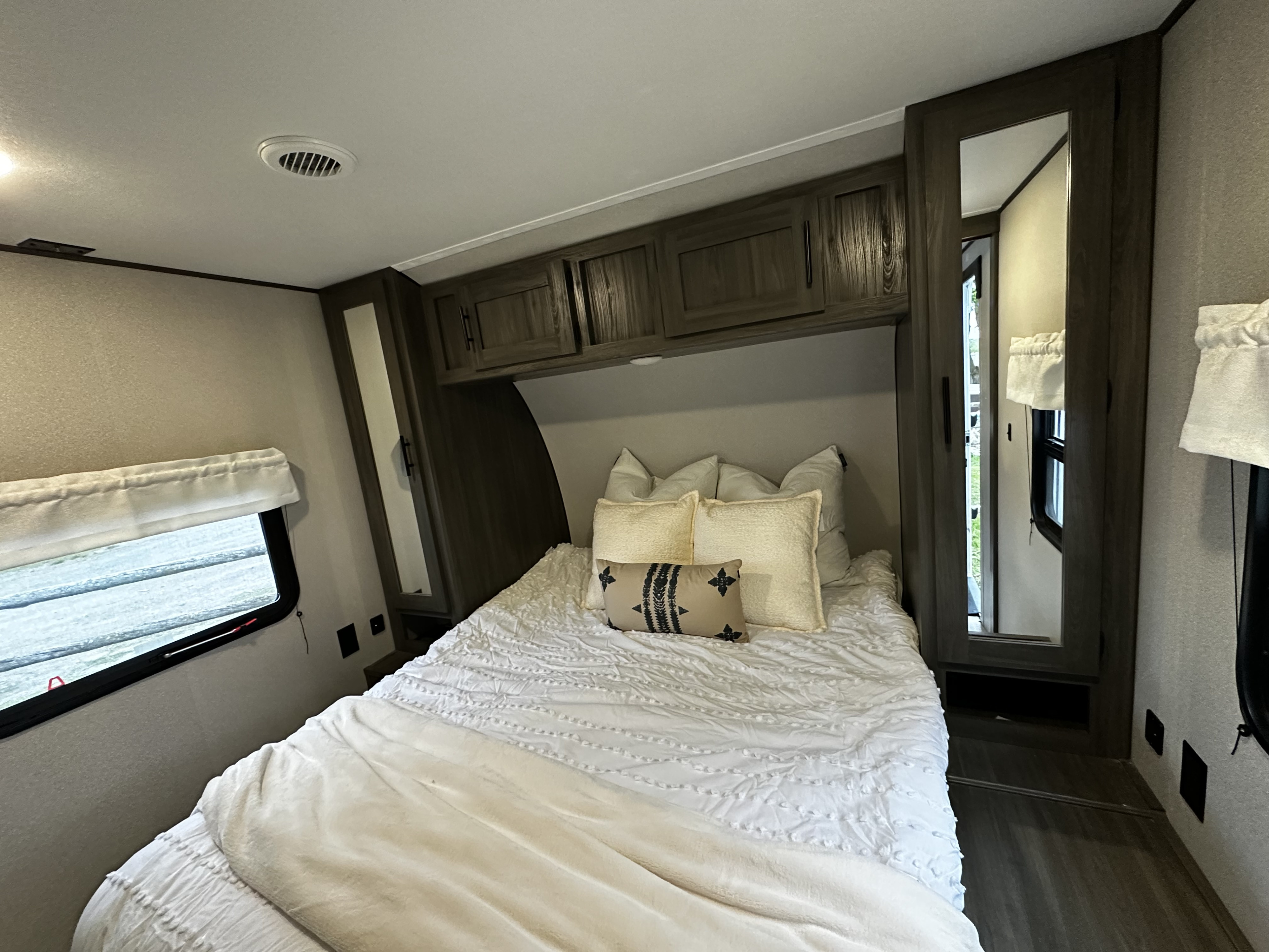 Compact RV rental bedroom featuring a bed, overhead cabinets, and a window for a cozy and functional space.. Forest River Grand River Comfortline 2021