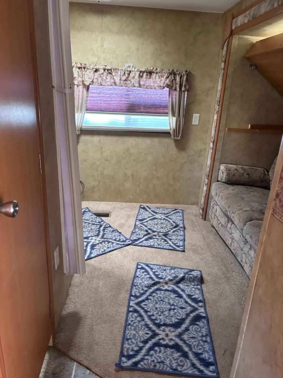 RV rental living area: Tan carpet, blue patterned rugs, patterned sofa, and a window. Typical camper interior view.. Keystone RV Cougar 2008