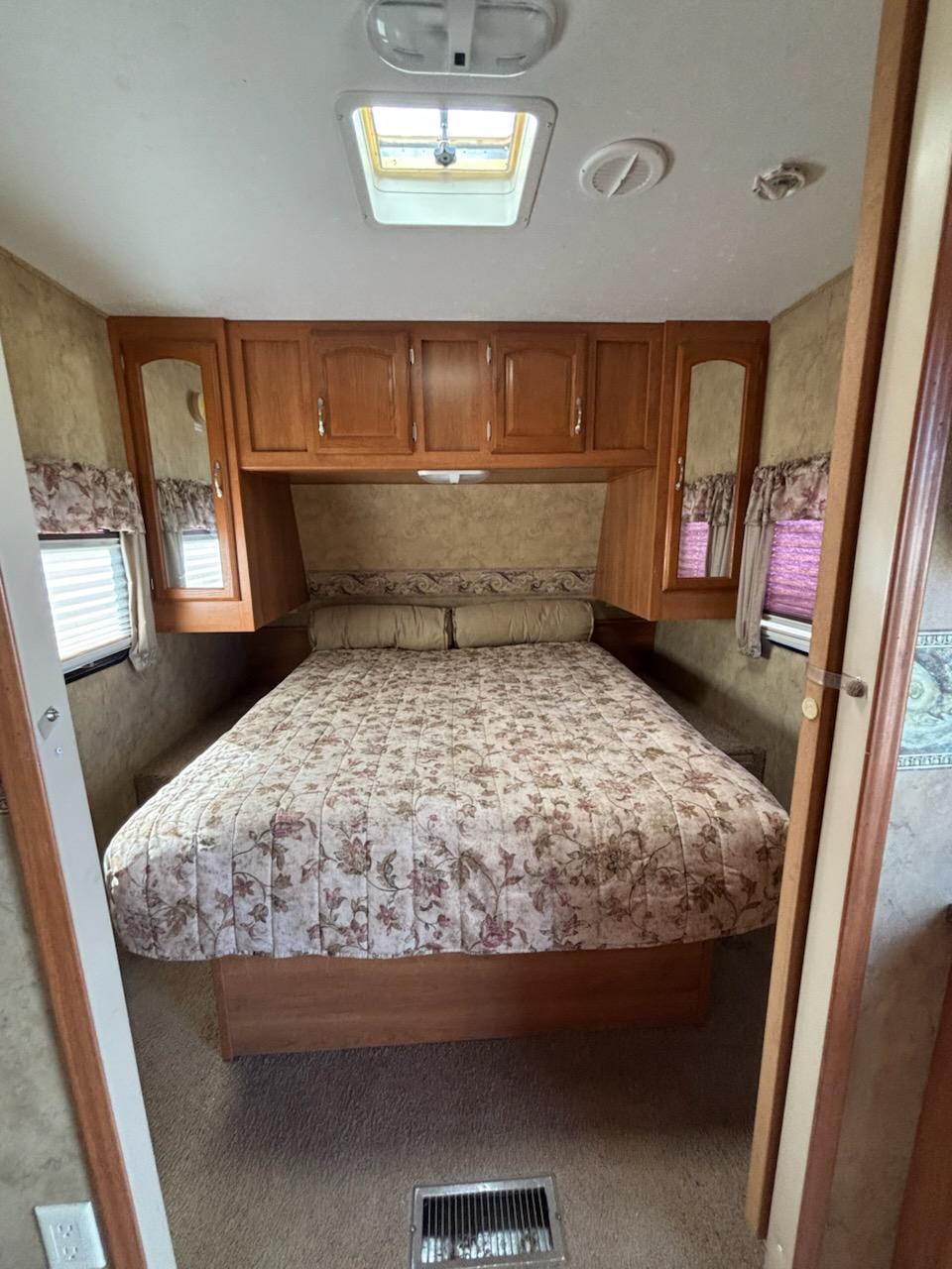 Cozy RV rental bedroom with floral bedding, ample wood storage, windows, and skylight for natural light.. Keystone RV Cougar 2008