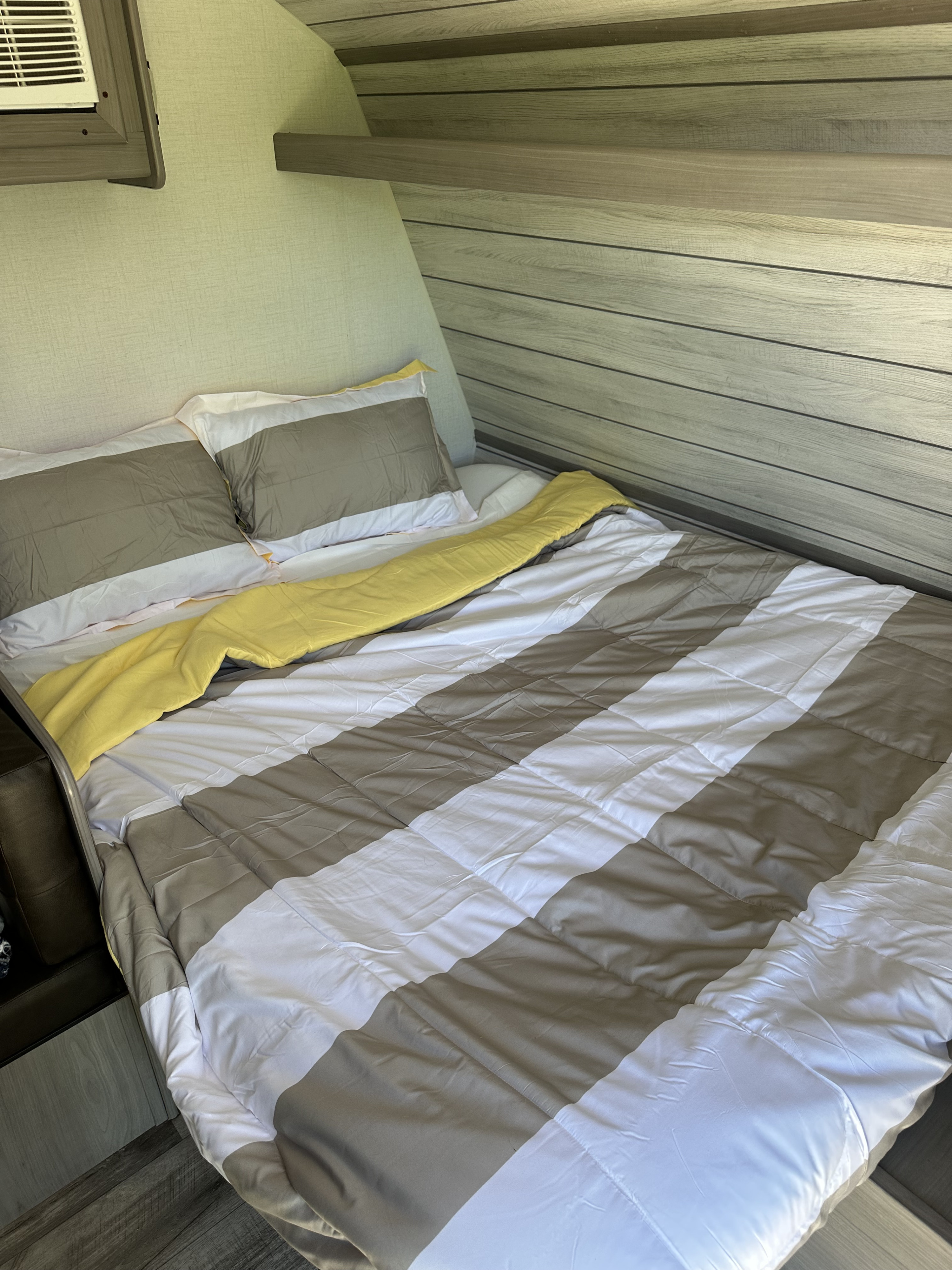 Cozy RV rental bed with grey/white striped comforter and yellow throw, showing modern RV interior details.. Dutchmen Coleman Lantern LT 2024