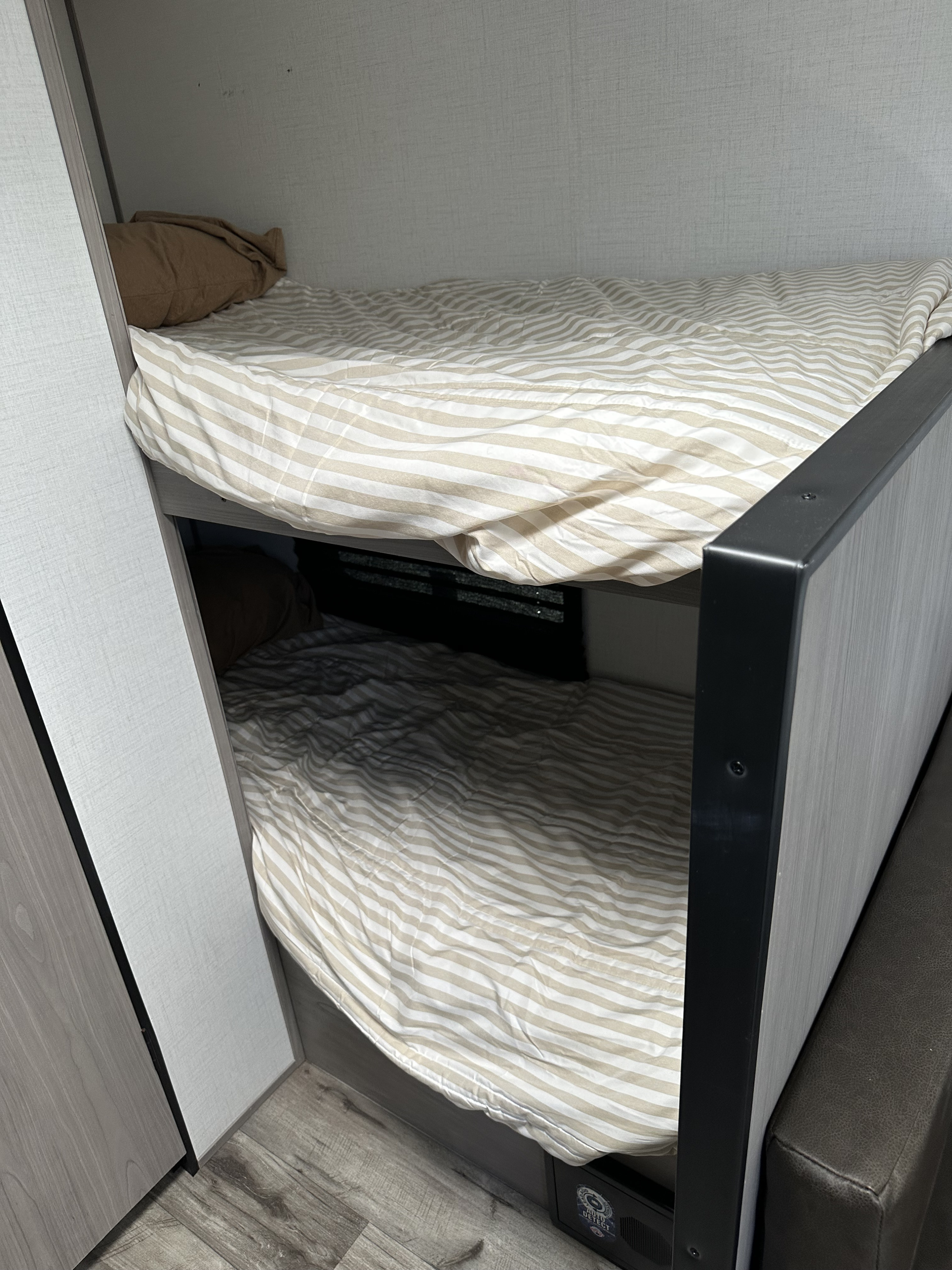 Compact RV rental interior featuring two made bunk beds with striped bedding and a brown pillow on the top bunk.. Dutchmen Coleman Lantern LT 2024