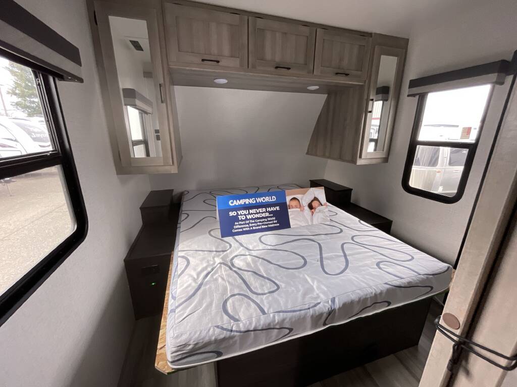 This cozy RV bedroom interior, perfect for an RV rental, features a comfortable bed, overhead storage, and dual windows.. Winnebago Voyage 2022