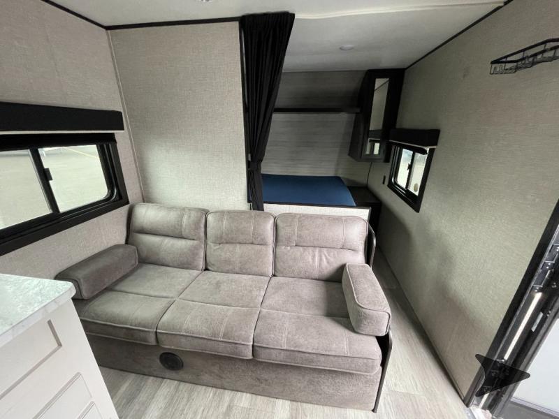 Inside this modern rv rental: a compact living space featuring a comfortable gray sofa, a sleeping area with a bed, and windows.. Jayco Jay Flight SLX 2022