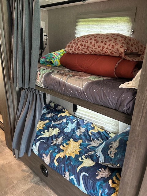 RV rental interior: two cozy bunk beds with space and dinosaur bedding, privacy curtains, and window blinds.. Coachmen Pursuit 31bh 2023