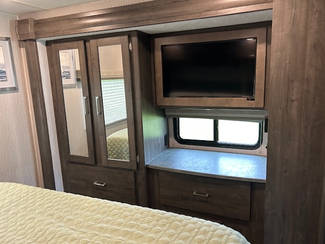 RV rental bedroom with mirrored wardrobe, built-in TV over window, and storage. Ideal travel trailer interior for your trip.. Coachmen Pursuit 31bh 2023