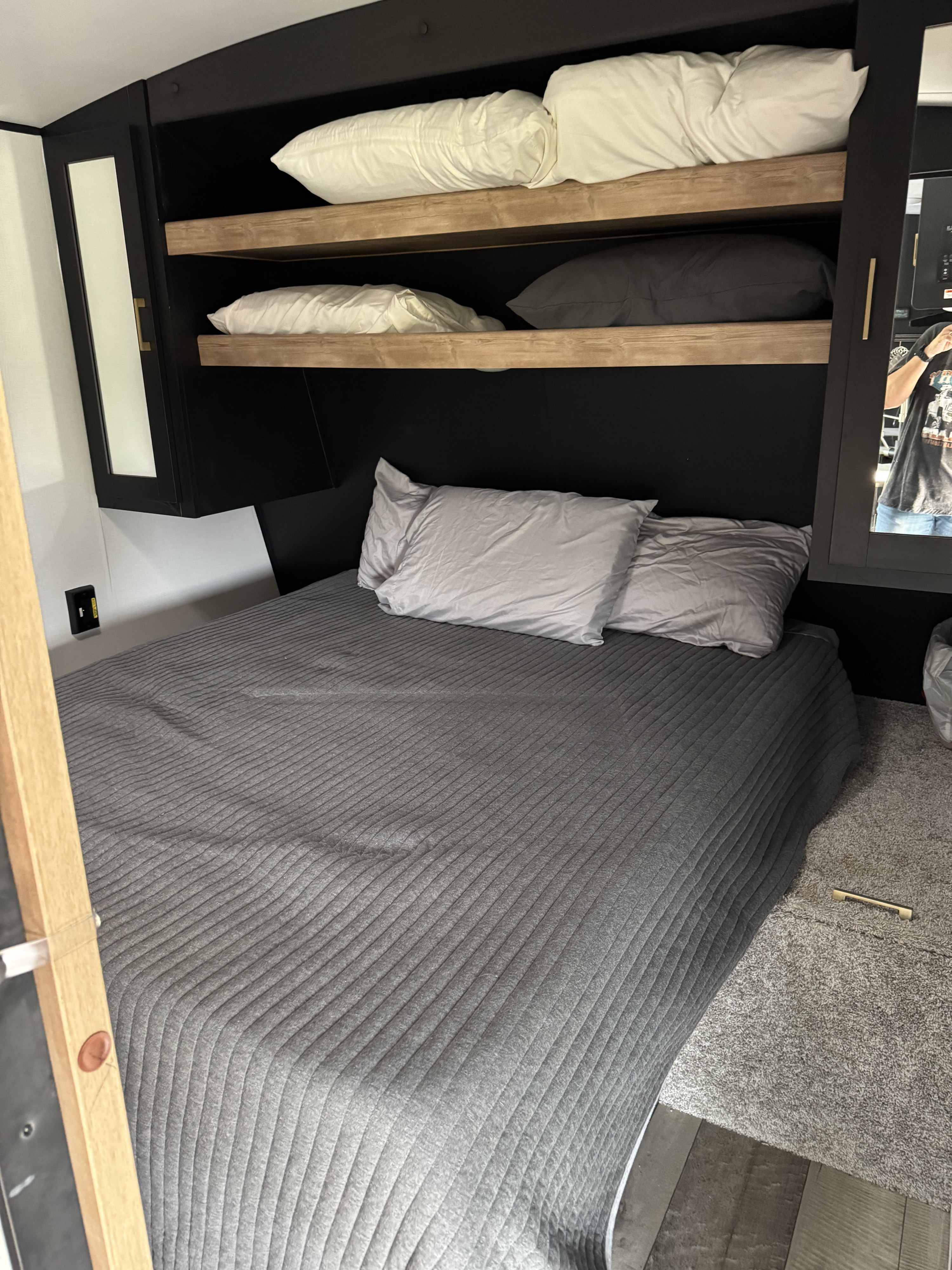 Modern RV rental bedroom. Features a cozy grey quilted bed, light & dark pillows on built-in shelves, and compact design.. Keystone RV Springdale 2022