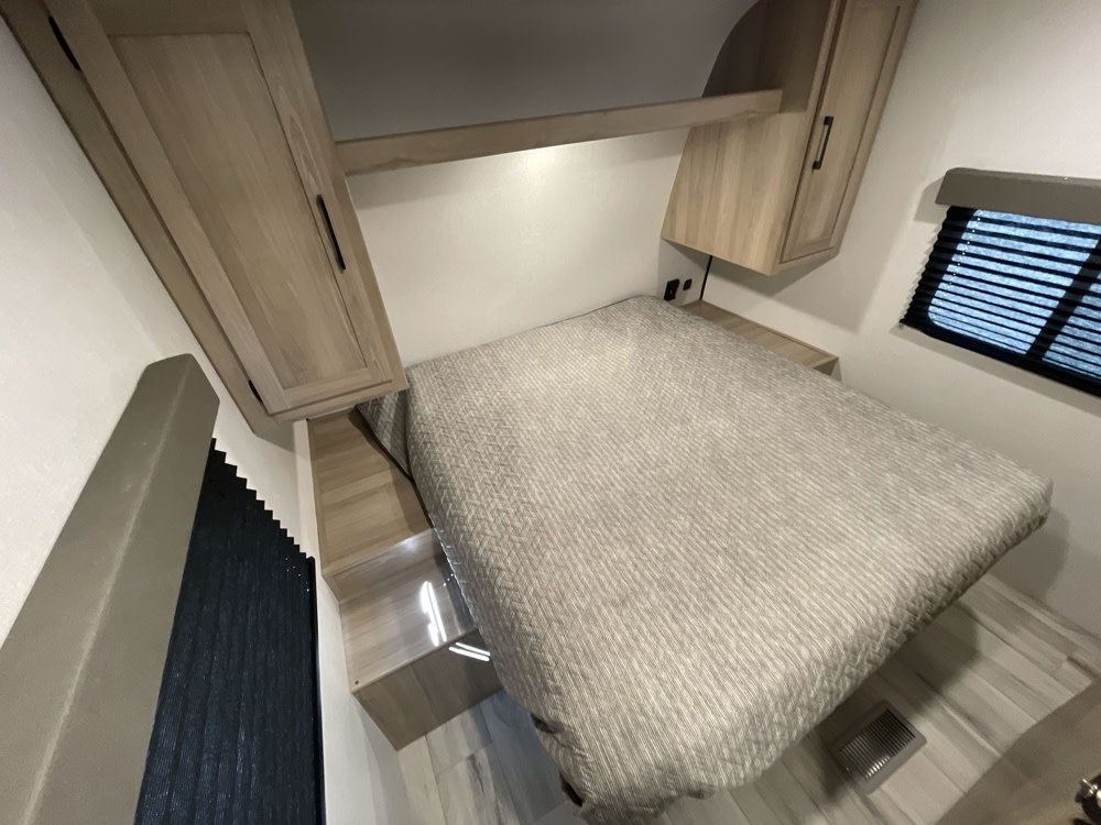 RV rental bedroom: a cozy interior with a striped bed, overhead cabinets, and window blinds.. Keystone Coleman Coleman Light 22 BX 2025