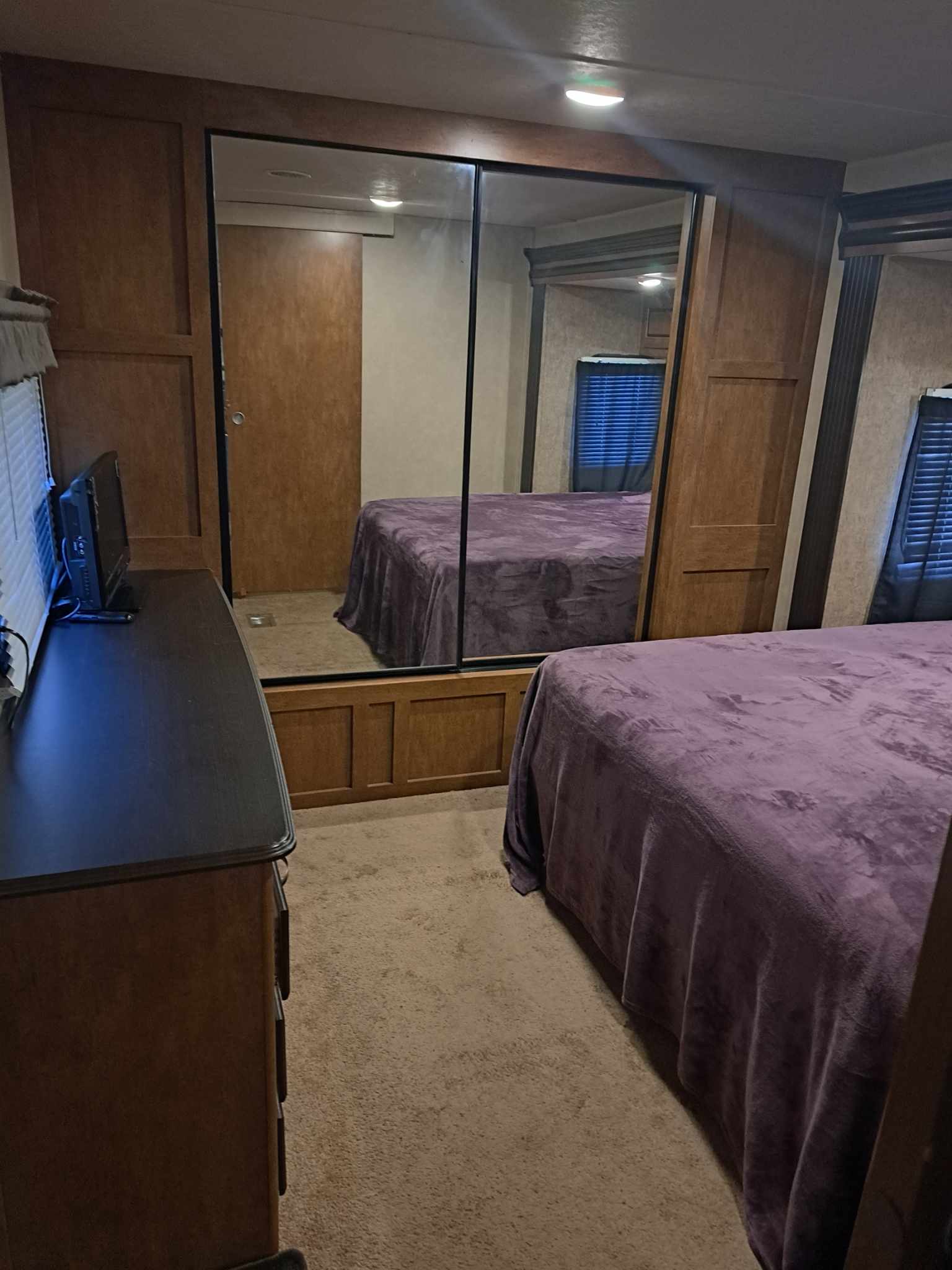 Cozy RV rental bedroom features a large mirrored closet, purple-blanketed bed, and TV on a dresser, perfect for travelers.. Forest River Wildwood 2016