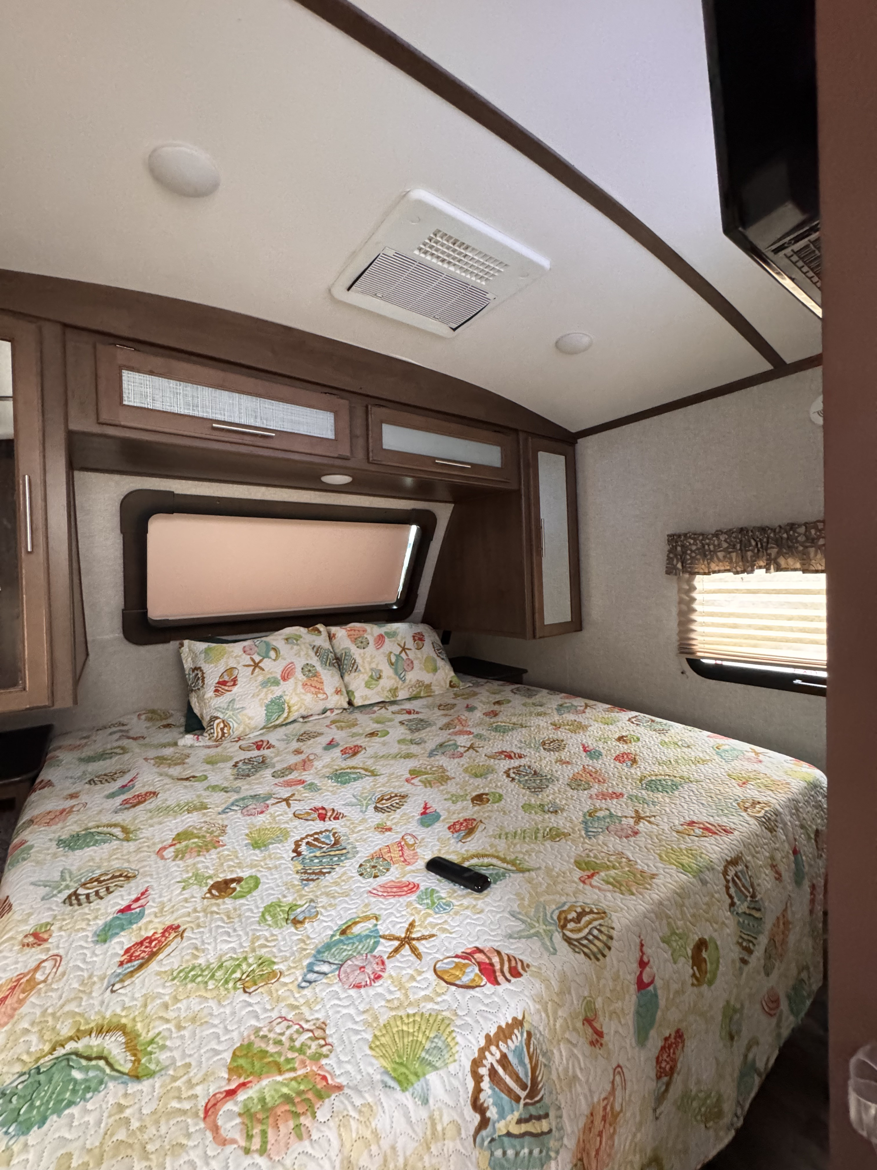 RV rental: Cozy bedroom featuring a seashell-patterned quilt, overhead cabinets, and ceiling AC.. Keystone RV Cougar 2019