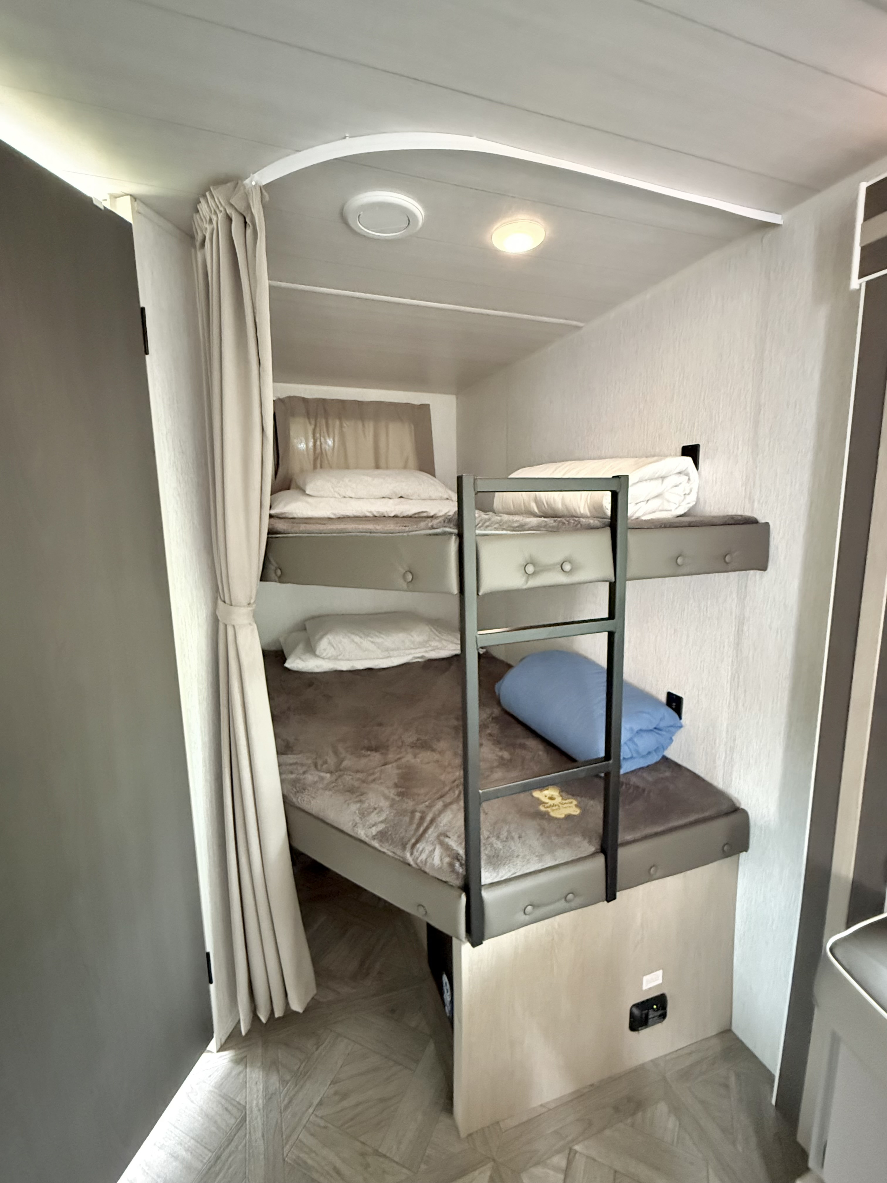 Cozy RV rental bunk beds, offering two sleeping areas, a ladder, and privacy curtain. Ideal for comfortable travel.. Forest River Wildwood X-Lite 2023