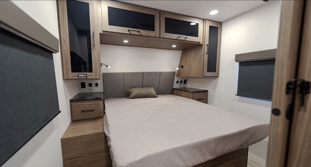 Comfortable RV rental bedroom featuring a cozy bed, ample overhead storage, bedside tables, and reading lights.. Alliance 262RB 2024