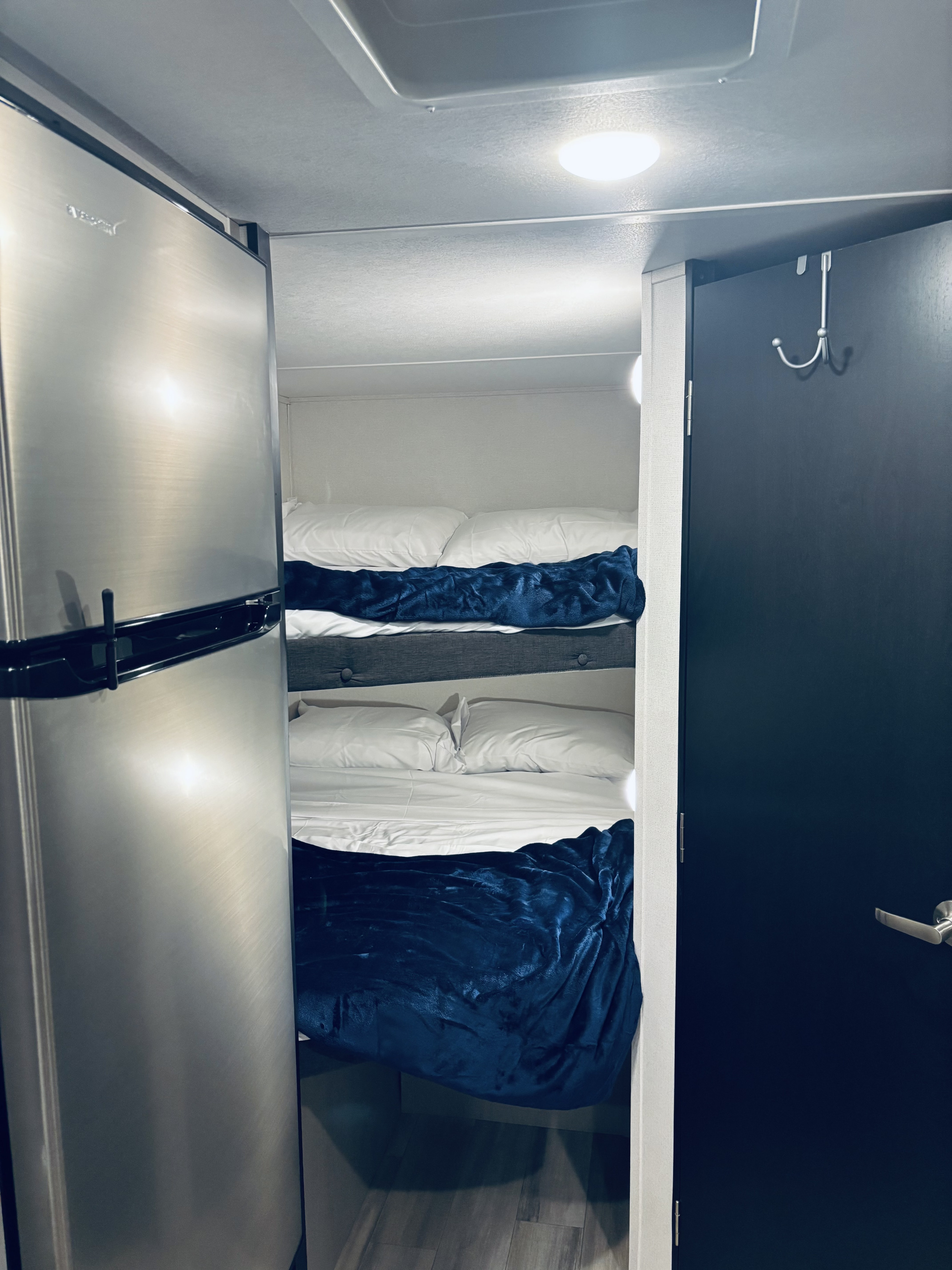 Explore this RV rental's clever interior: spacious fridge, two cozy bunk beds with blue blankets, and a handy door hook.. Forest River Tracer 2022