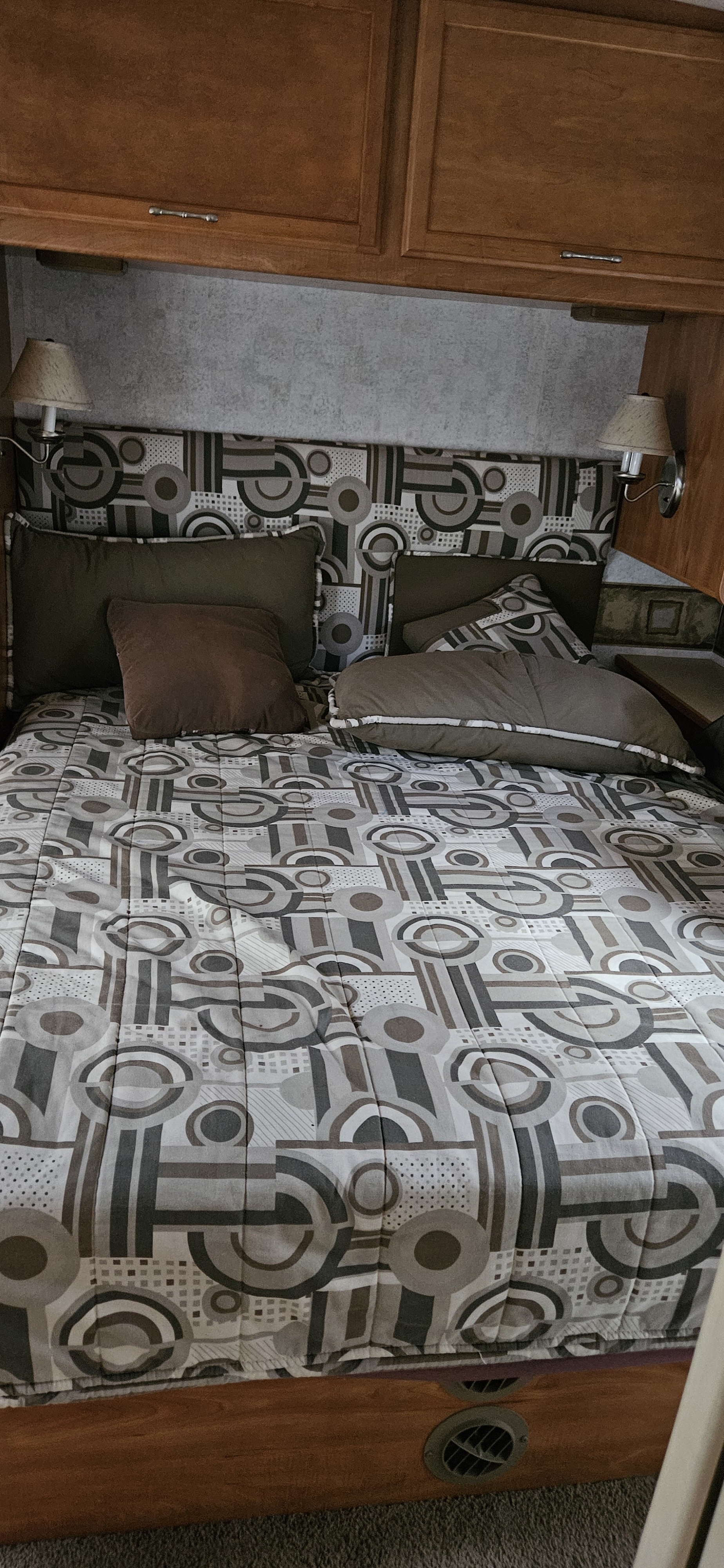 Comfortable RV rental bedroom featuring geometric bedding, overhead cabinets, and reading lamps. Ideal compact sleeping space.. Winnebago Sightseer 2006
