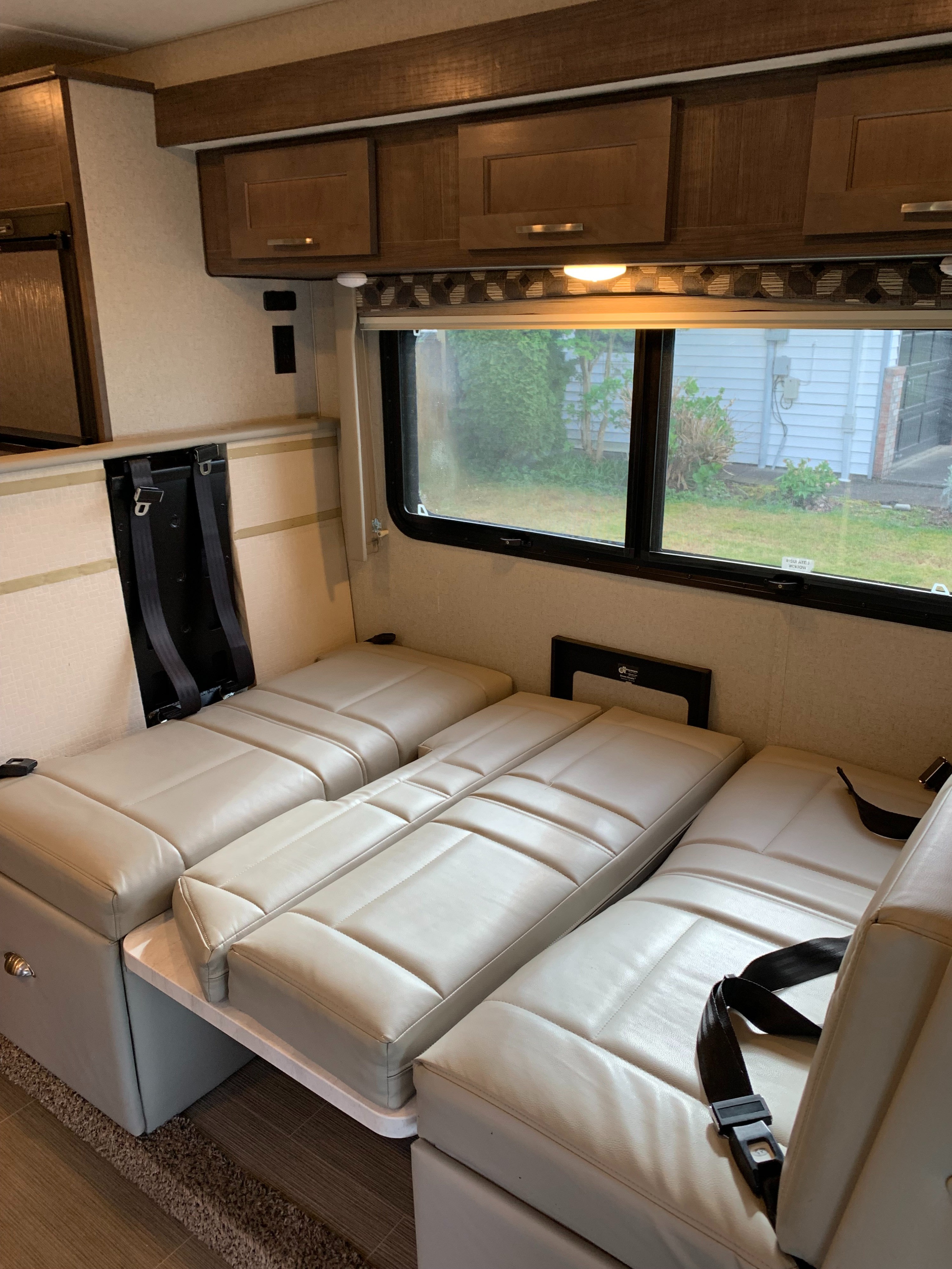 Spacious RV rental interior with light cream dinette seats converted into a bed, featuring seatbelts, wood cabinets, and a large window view.. Adventurer Adventurer Motorhome 2019