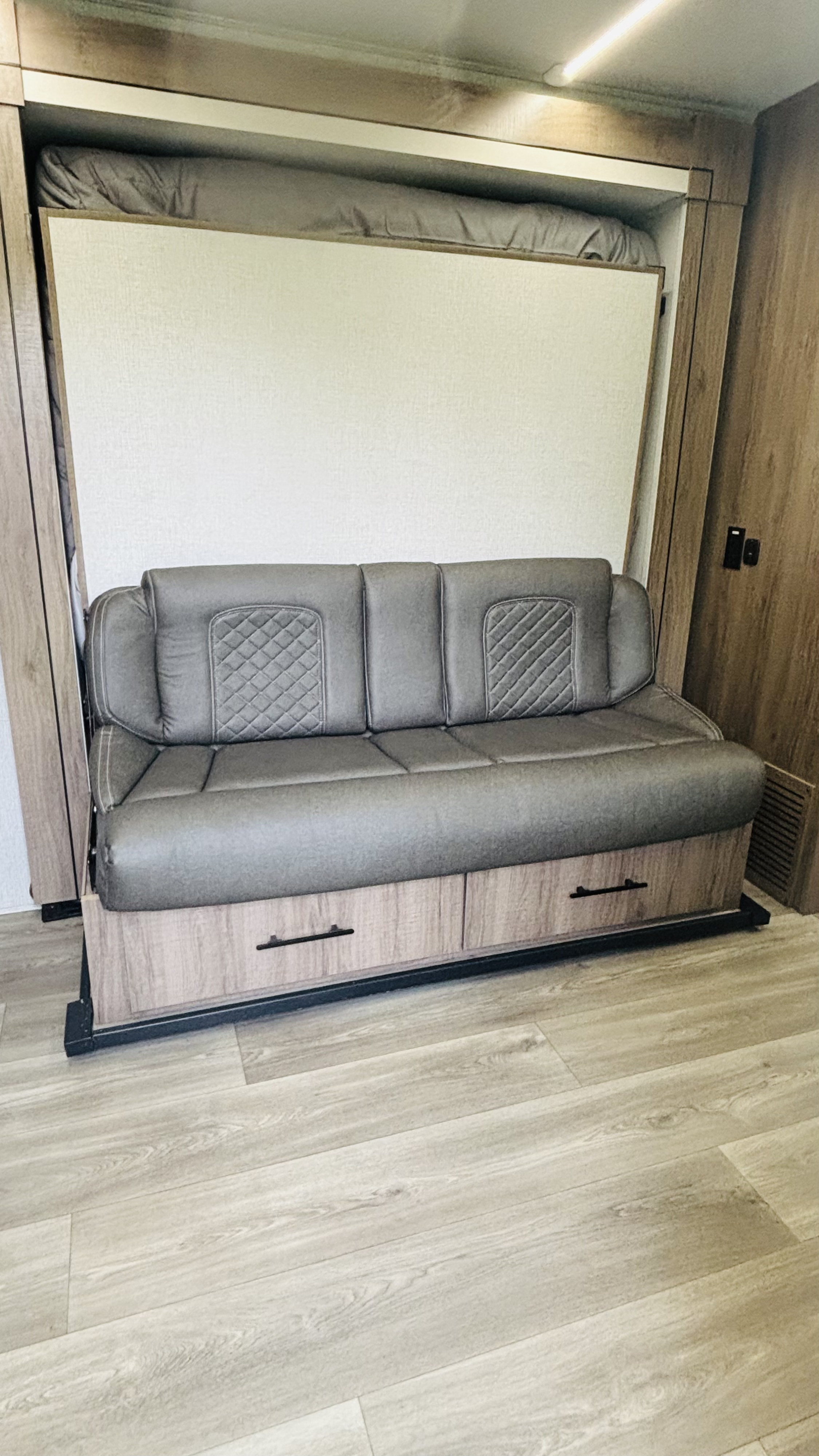 RV rental: Modern interior featuring a grey sofa, which conceals a pull-down bed above, and built-in storage drawers below.. Grand Design Imagine AIM 2024