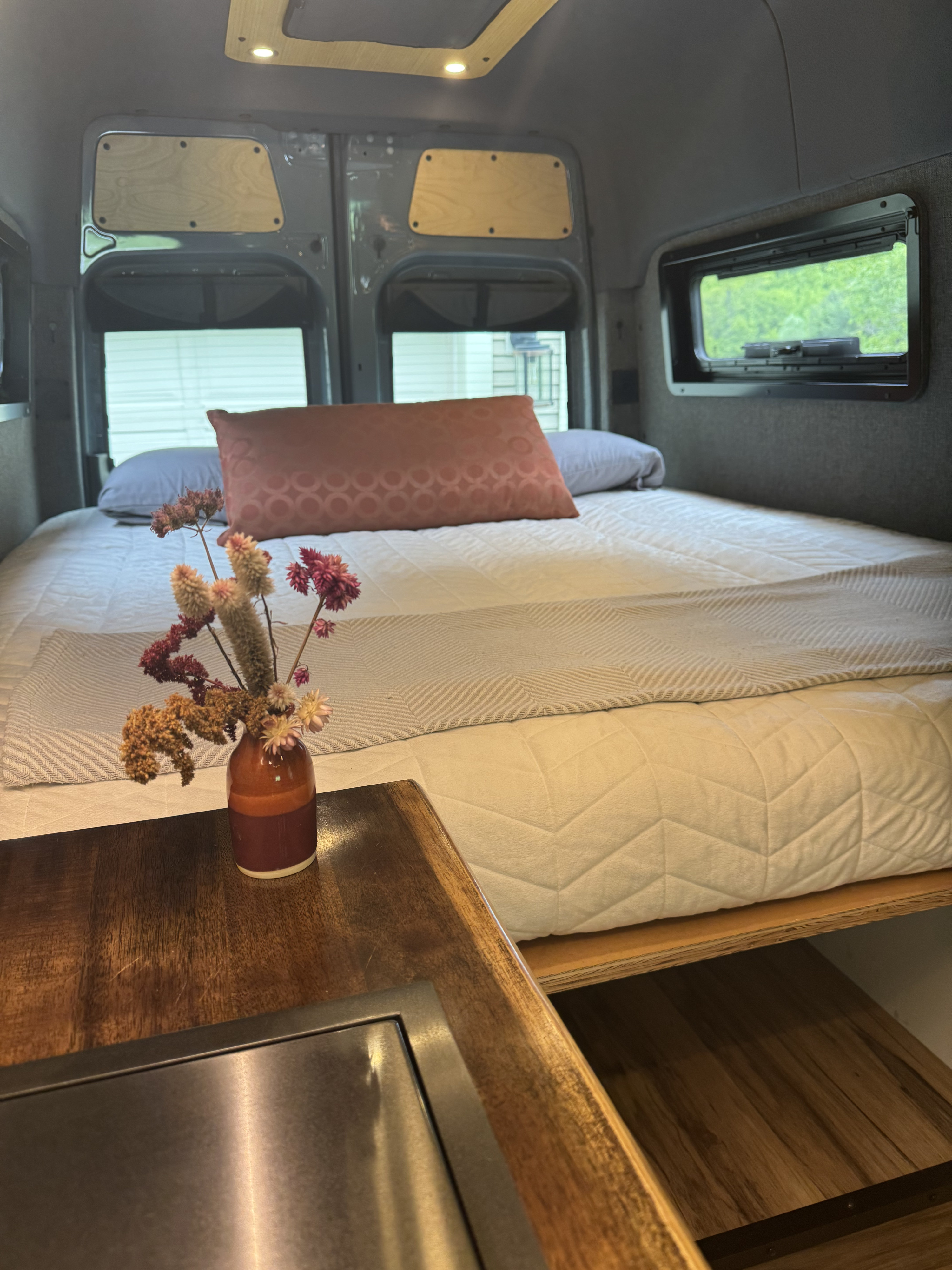 Relax in this well-appointed RV rental. A comfortable bed, warm wooden accents, and a touch of nature create a cozy travel space.. Mercedes-Benz Sprinter 2021