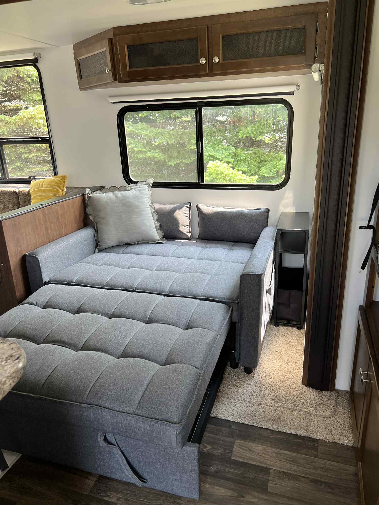 RV rental's inviting interior: gray sofa bed, large windows showcasing trees, and functional overhead cabinets.. Keystone RV Hideout 2016
